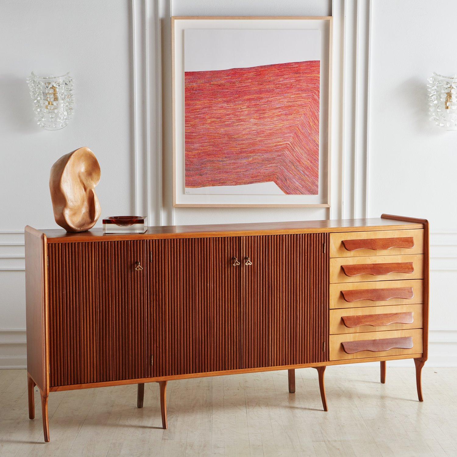 An extraordinary 1970s teak sideboard in the style of Paolo Buffa. This piece has three doors with fluted details and brass pulls, which open outwards to reveal two shelves. It has five birch drawers on the right hand side with curved teak handles.