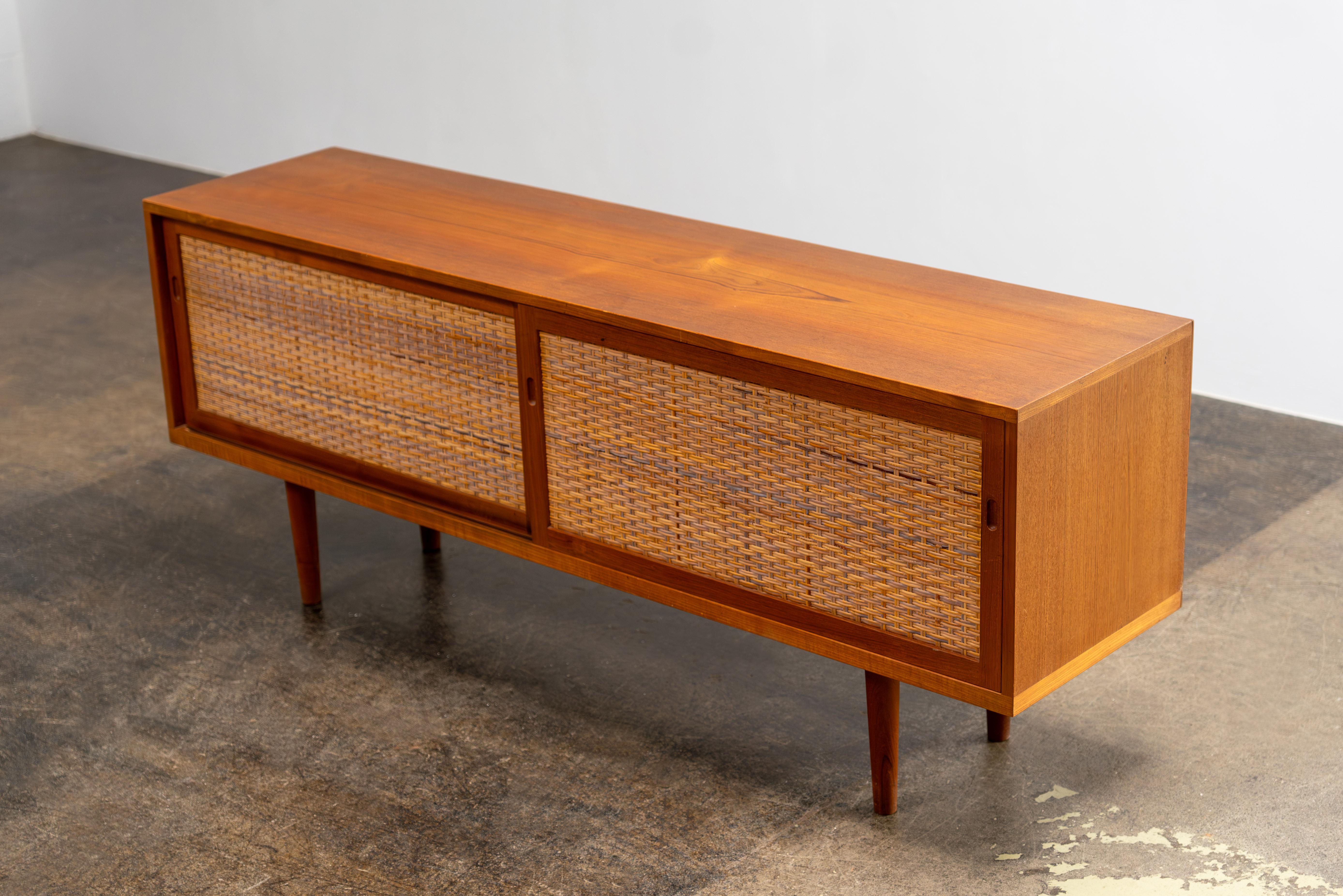 Credenza in teak e canna - Hans Wegner
Ry Møbler, anni '60

Elegante credenza, modello No. RY 26 di Ry Møbler, disegnata da Hans Wegner negli anni Sessanta. Realizzato in pregiato teak, presenta una venatura calda e vivace con un motivo di