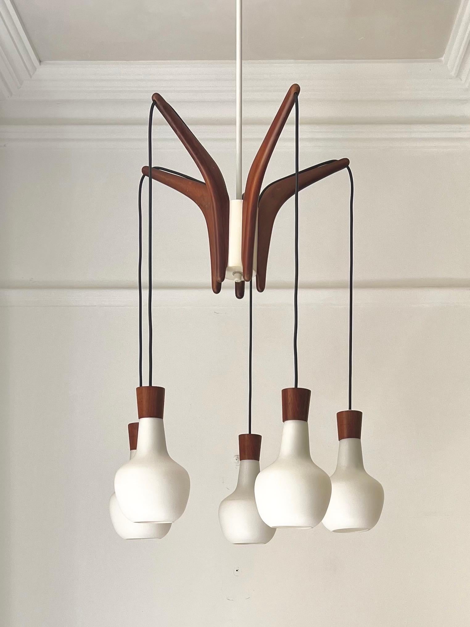 Un lampadario semplice ed elegante con una struttura in teak e cinque paralumi in vetro bianco opaco, molto simile allo stile di Uno & Östen Kristiansson della Svezia, ma senza marchio o etichetta.

Il lampadario è in buone condizioni vintage, con