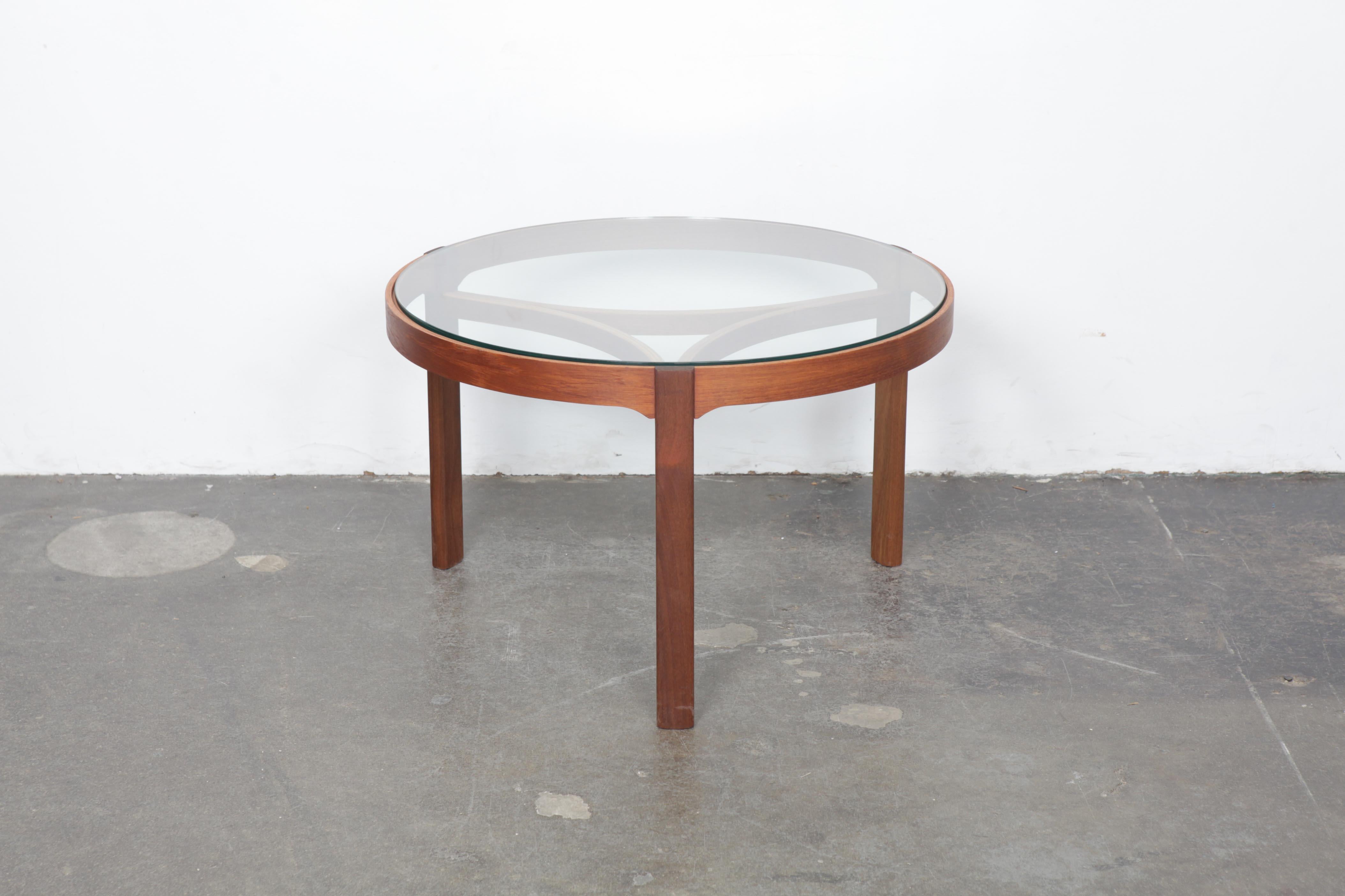 English circa 1960s teak and glass top round coffee table, it has been newly refinished and has a brand new glass top, produced by Nathan of England. Beautiful table with graceful curved leg supports exposed through the glass.