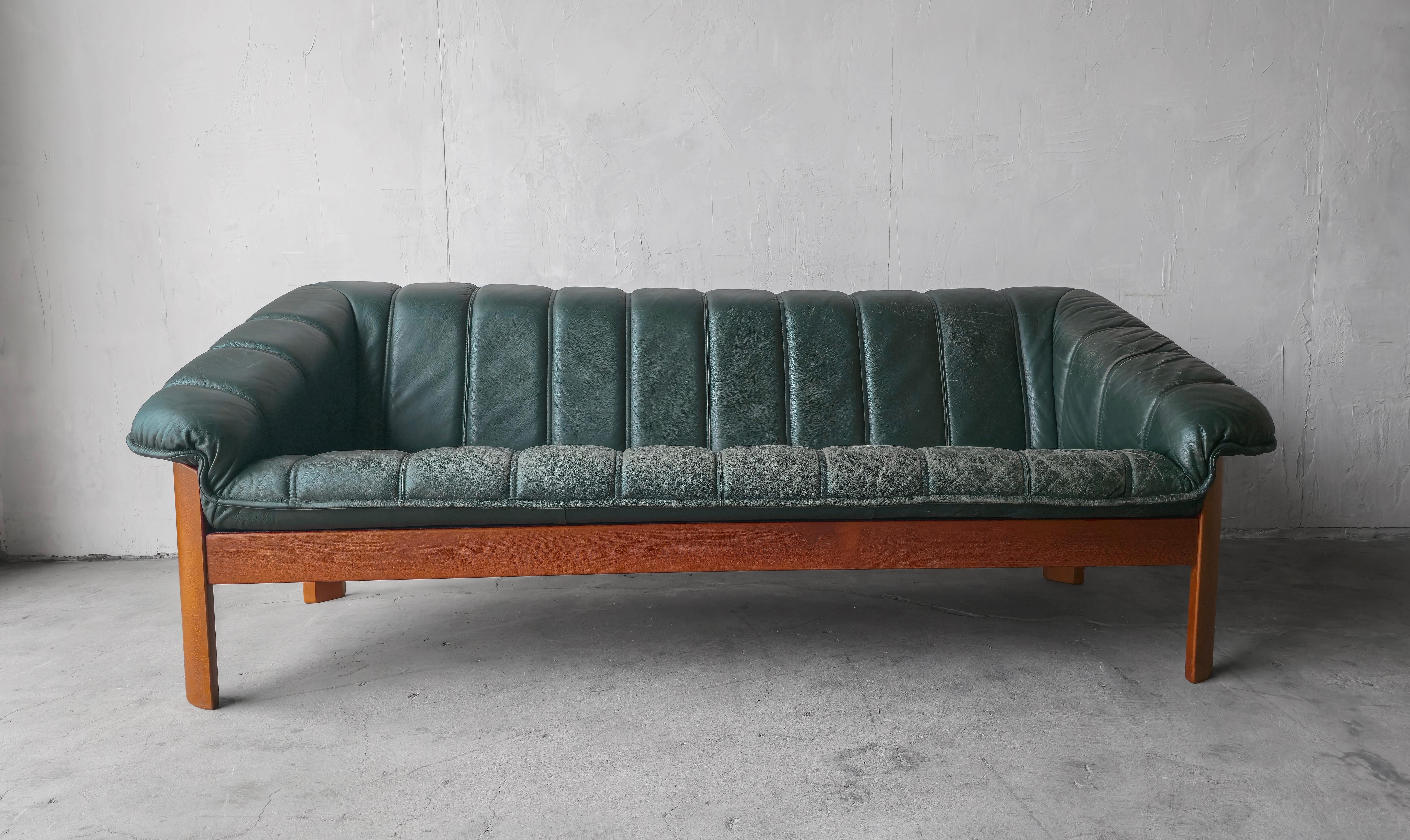 A perfect example of Scandinavian design.  This Hjellegjerde sofa oozes style and craftsmanship, it features a channeled bucket style seat in dark forest green leather with nice patina and a substantial teak frame.  This sofa has a very modern feel,