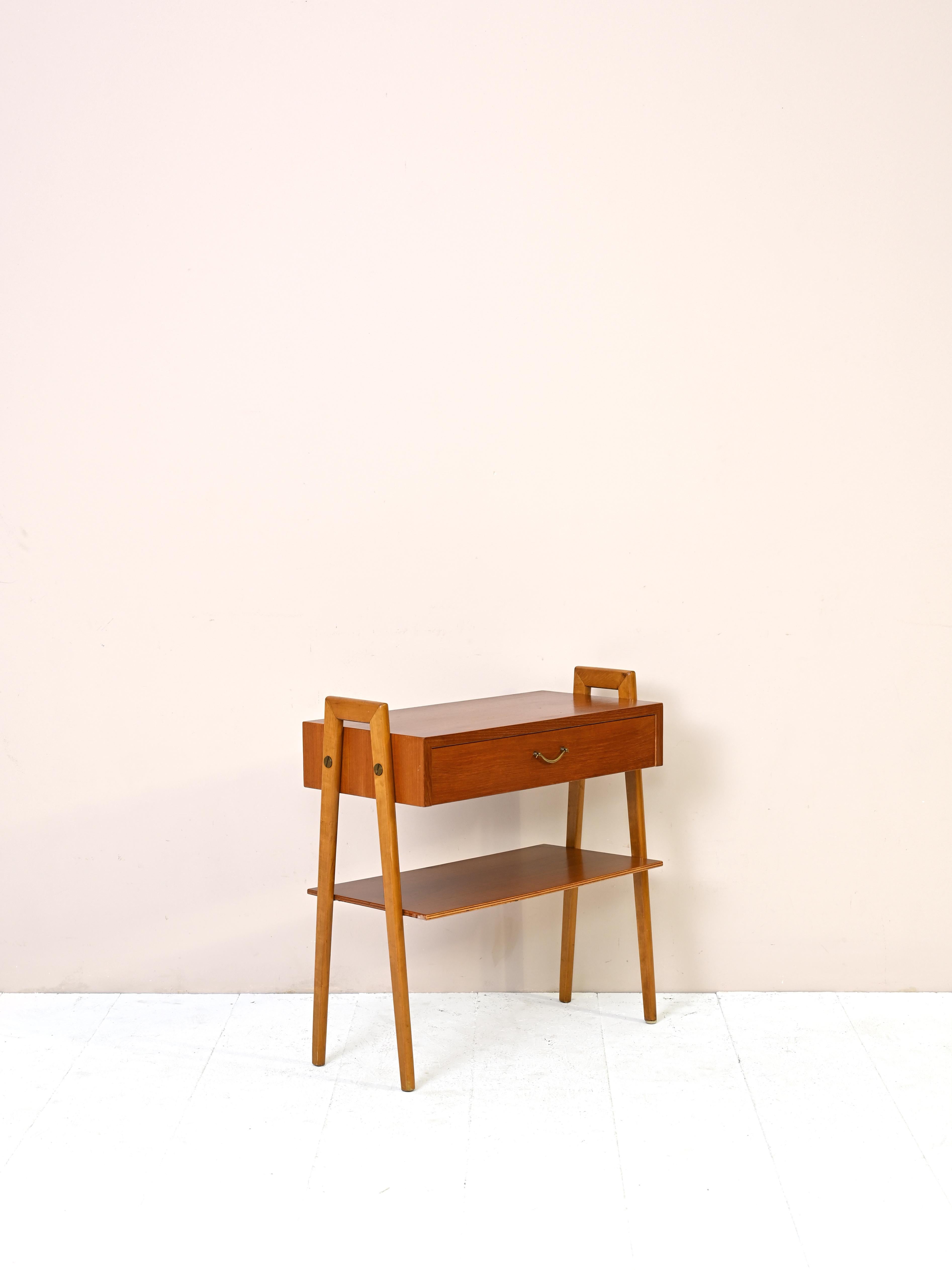 Original nightstand from the 1960s of Scandinavian manufacture.
This cabinet, ideal for the bedroom but also for the entryway or hall, features a
drawer with a metal handle and a magazine rack top.
Its peculiarity lies in the unusual shape of the