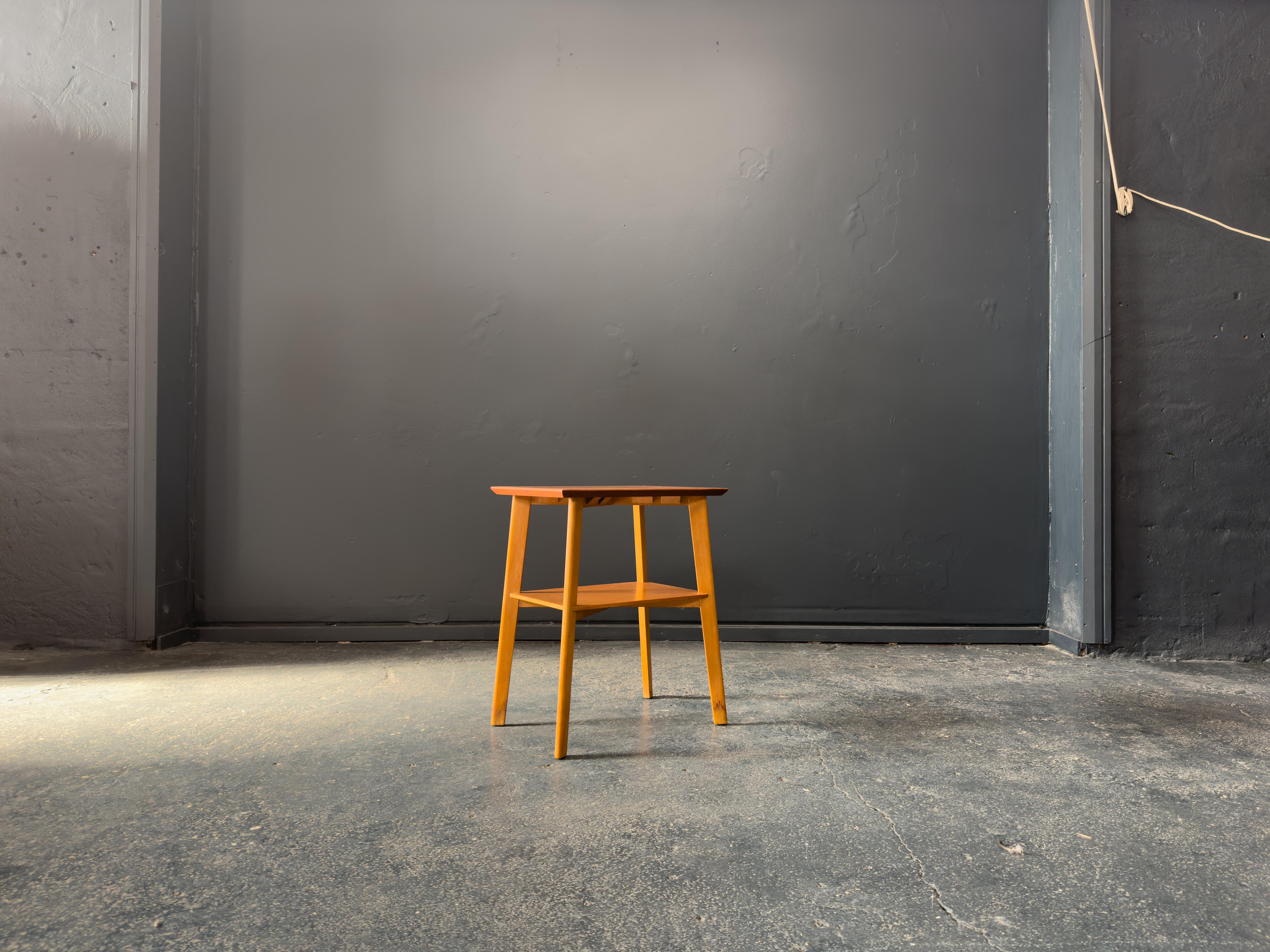 This elegant teak and oak side table captures the minimalist beauty and functional ethos of mid-century design. Featuring a sleek, rectangular teak top with softly bevelled edges, the table showcases the warm, golden hues and rich grain