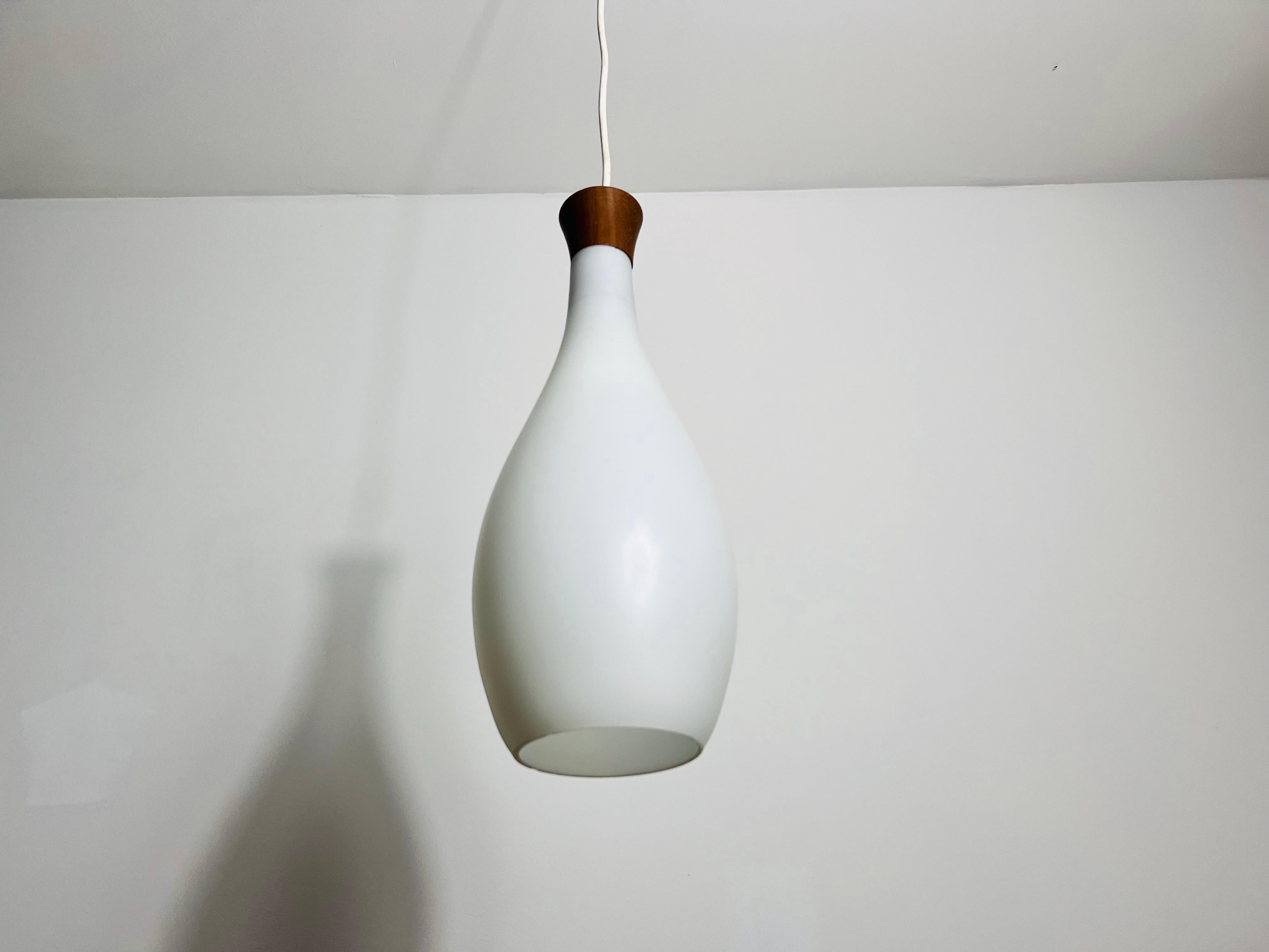 Questa elegante lampada a sospensione, disegnata da Uno & Östen Kristiansson per Luxus Sweden negli anni '60, incarna il design moderno di metà secolo. Presenta un elegante braccio in teak e un paralume in vetro opalino, per un'estetica sofisticata