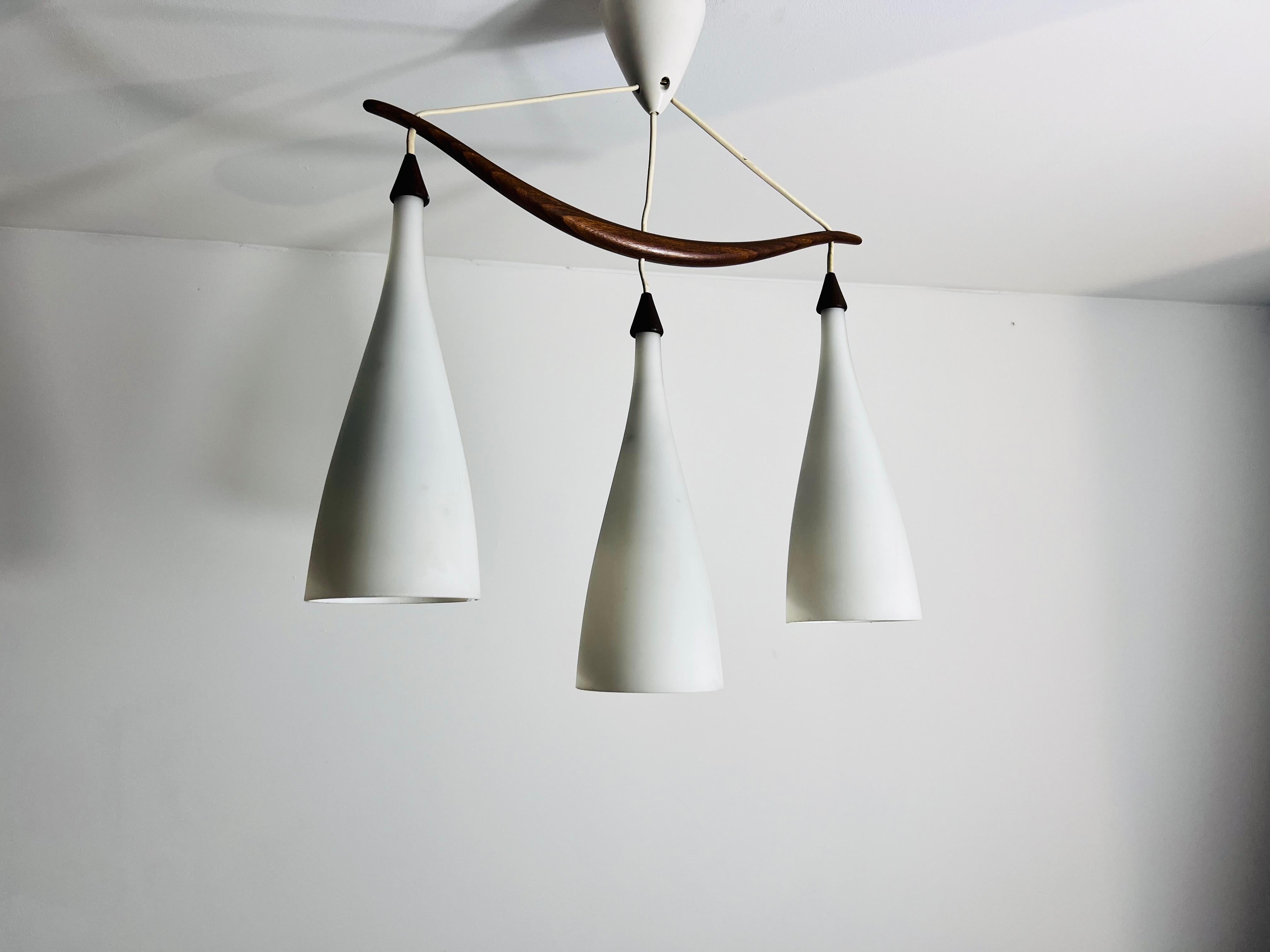 This elegant pendant lamp, designed by Uno & Östen Kristiansson for Luxus Sweden in the 1960s, epitomizes mid-century modern design. It features a sleek teak arm and three opal glass shades, providing a sophisticated and high-quality aesthetic. Its