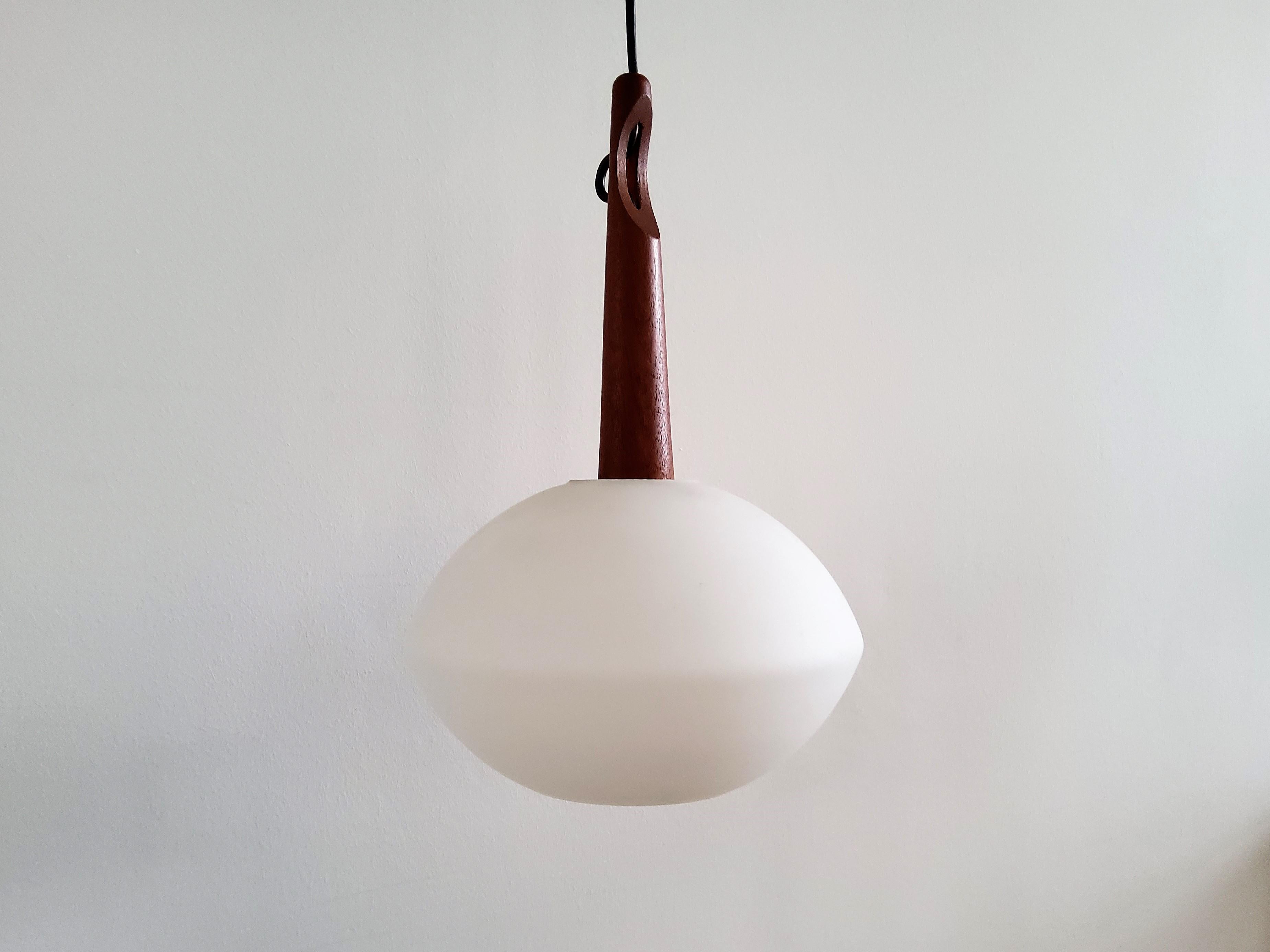 Cette lampe suspendue très élégante a été conçue par Uno et Östen Kristiansson pour Luxus en Suède dans les années 1950. Il est doté d'un abat-jour en verre opalin et d'une suspension en bois de teck. Il donne une belle lumière chaude lorsqu'il est