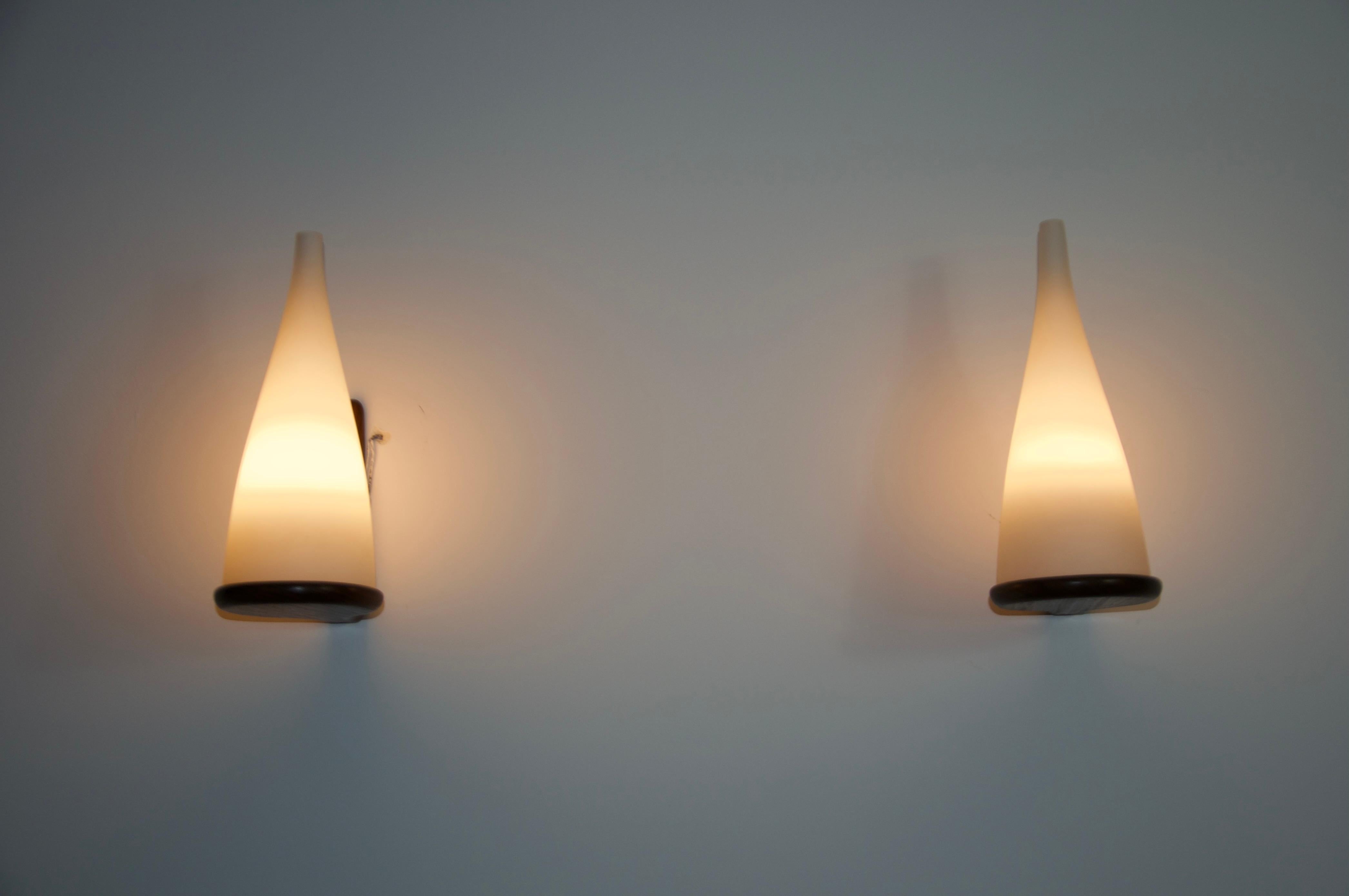 This elegant pair of wall lamps, designed by Uno & Östen Kristiansson for Luxus Sweden in the 1960s, epitomizes mid-century modern design. It features a sleek teak arm and an opal glass shade, providing a sophisticated and high-quality aesthetic.