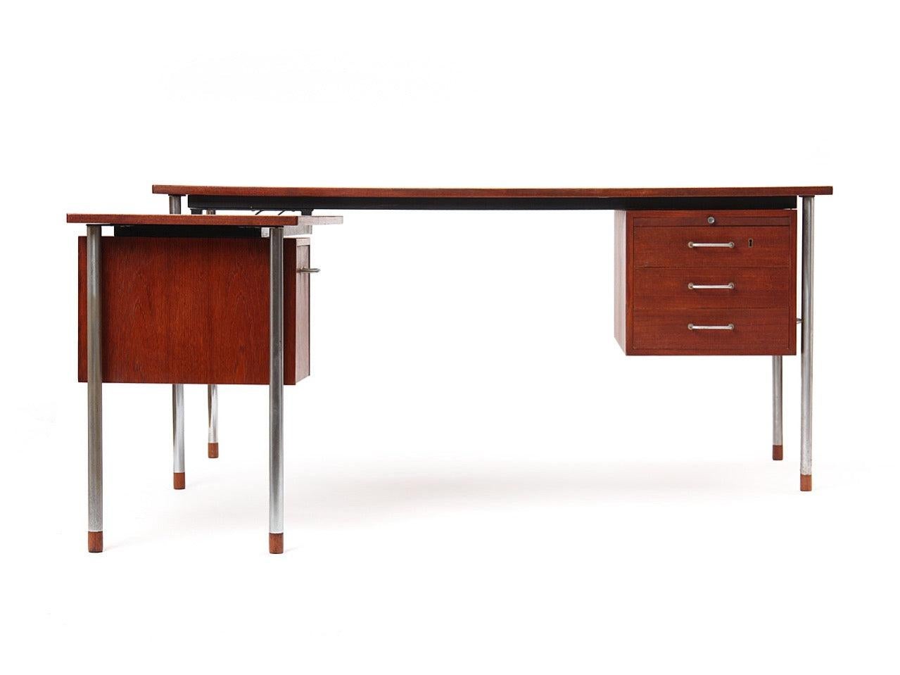 Una scrivania in teak con struttura in acciaio e tiranti, con un ripiano laterale sinistro che ospita scaffali per l'archiviazione. Dimensioni del ritorno: 39,5
