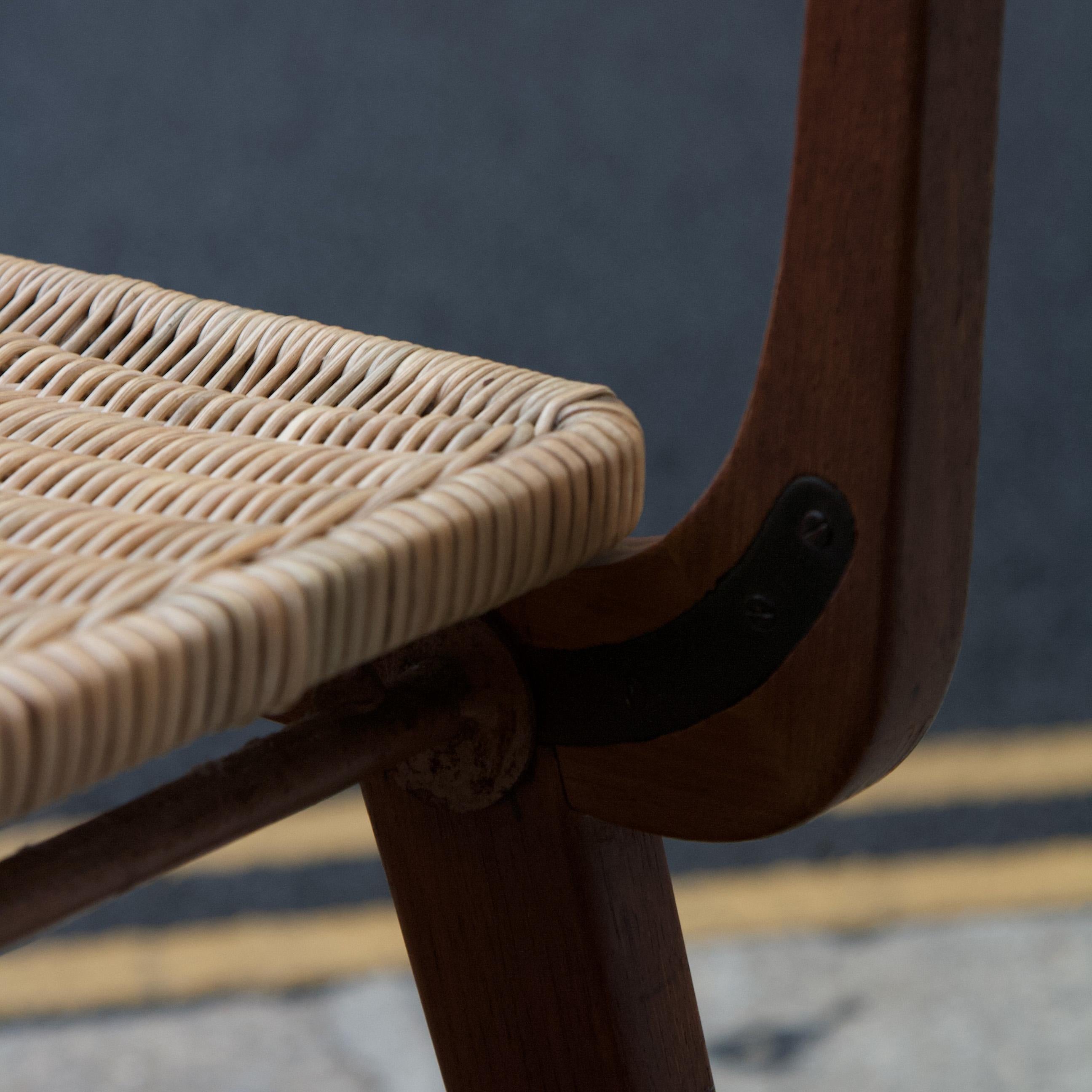 A teak chair, likely to have been made in France during the early 1950s. 

The seat and back of this chair are wicker, woven around a steel frame which is fixed to the teak body of the chair. The curved wooden body is formed by several pieces of