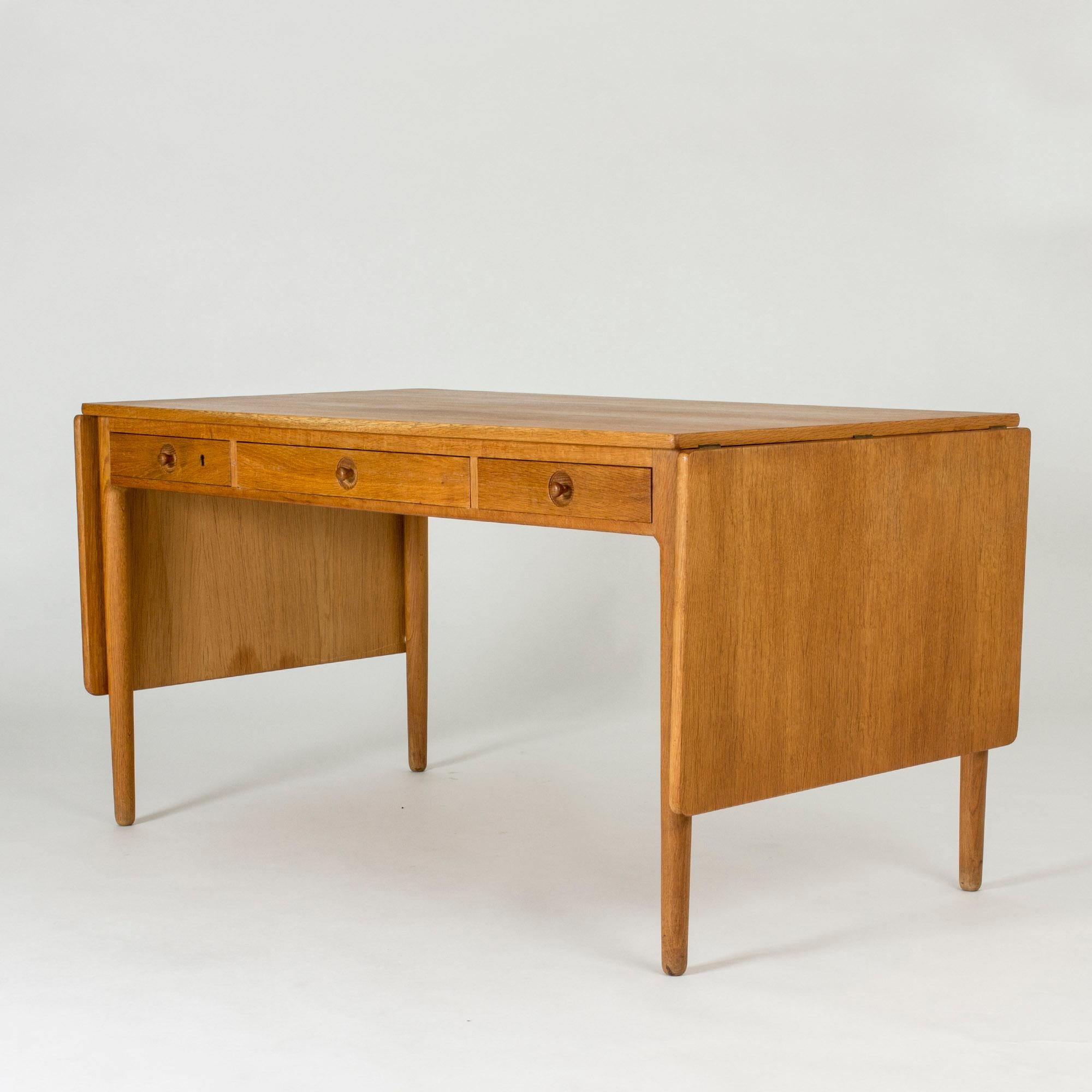 Desk by Hans J. Wegner made from oak. Two drop leaves make it possible to extend the desk to 232 cm, making it easy to use as a conference table. Three drawers with charming sculpted knobs. One of the drawers has a carefully executed inset for