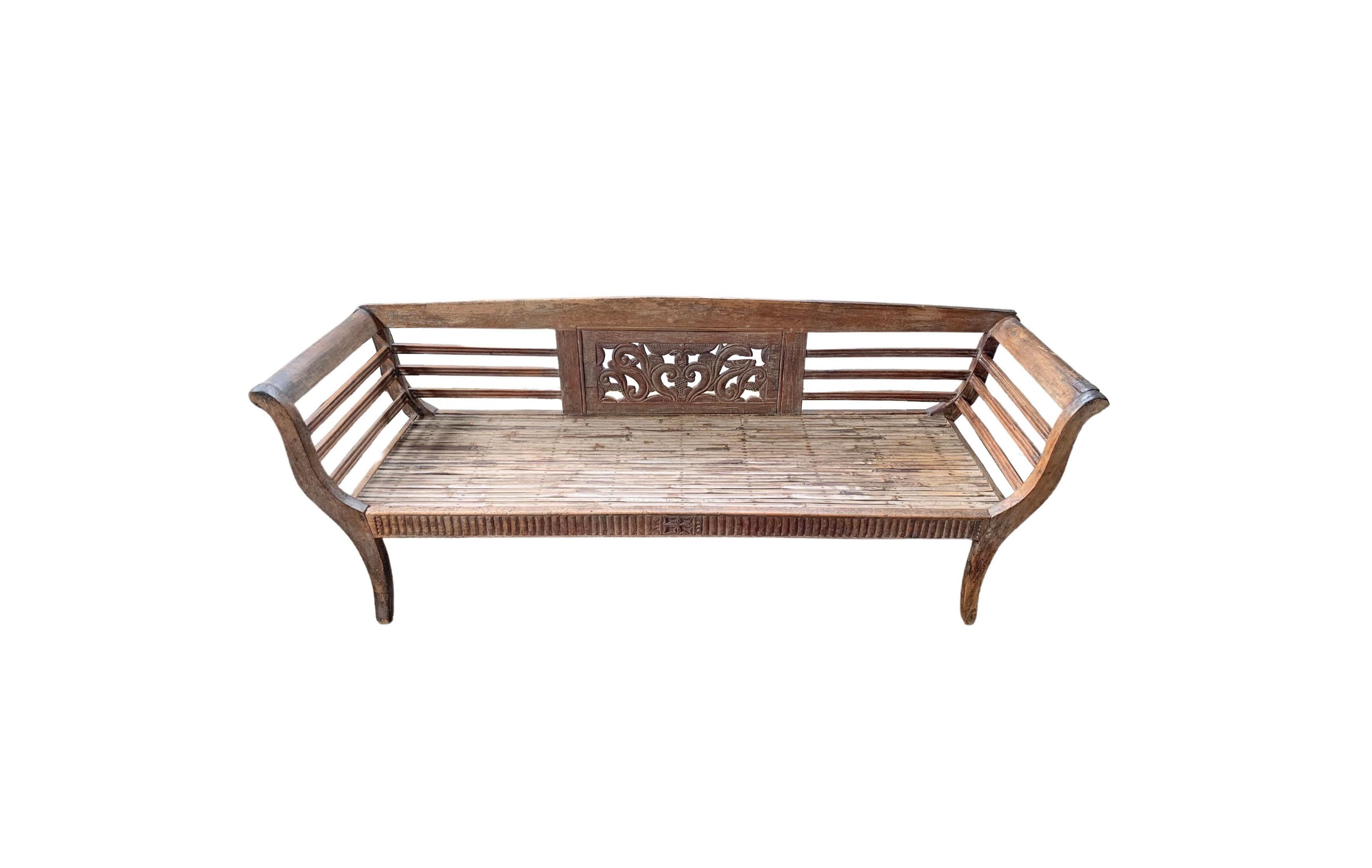 This hand-carved teak wood bench originates from the Island of Madura, off the coast of Northeastern Java. It features a wonderful array of carved detailing along its frame which includes floral engravings. The seat is crafted from long bamboo