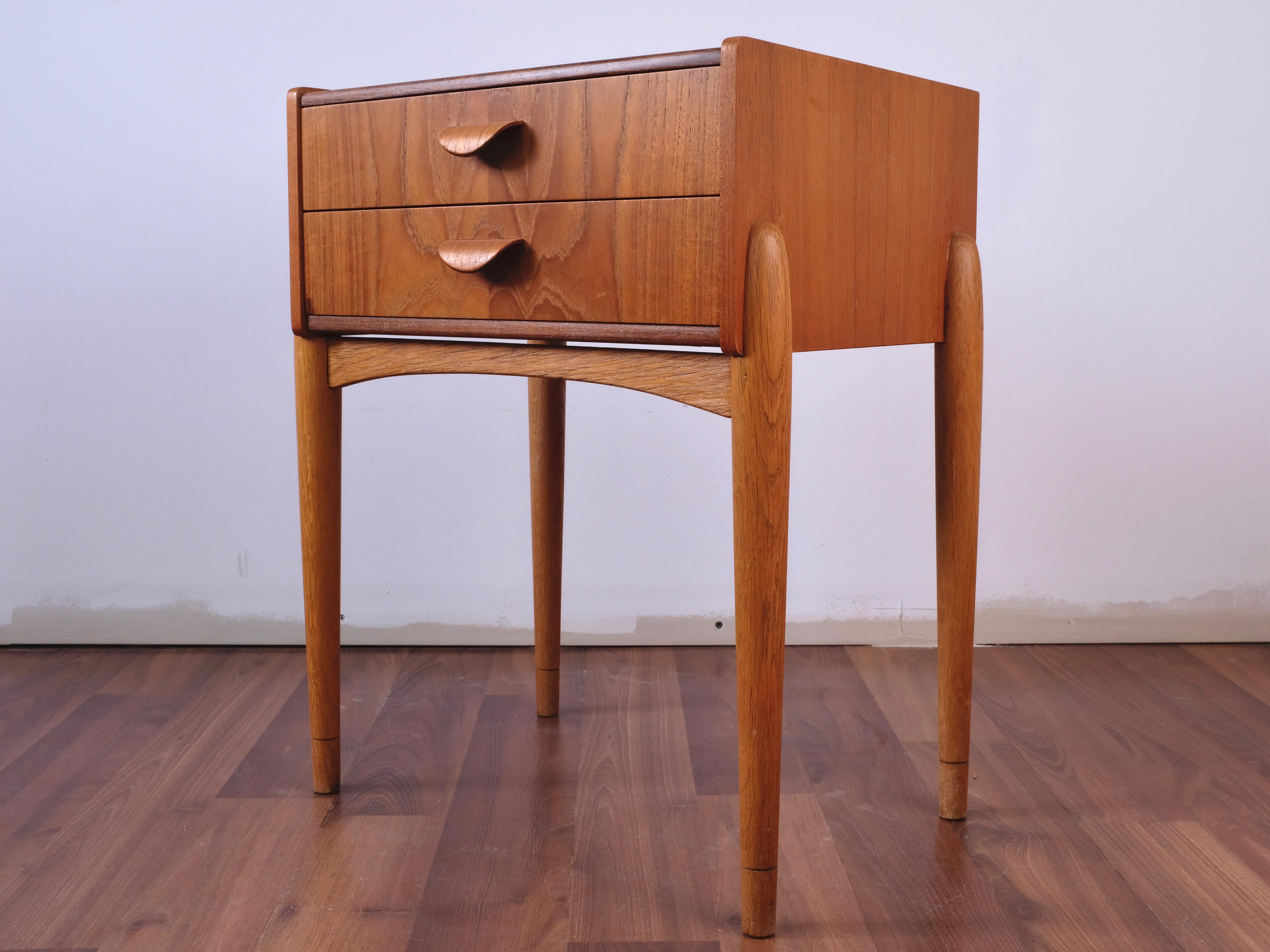 A beautiful teak bedside table with 2 drawers and curved molded teak handles. Very unique and visually as well as functionally attractive. Its 4 white oak dowel legs completes its authentic Mid-Century Modern visual appearance.