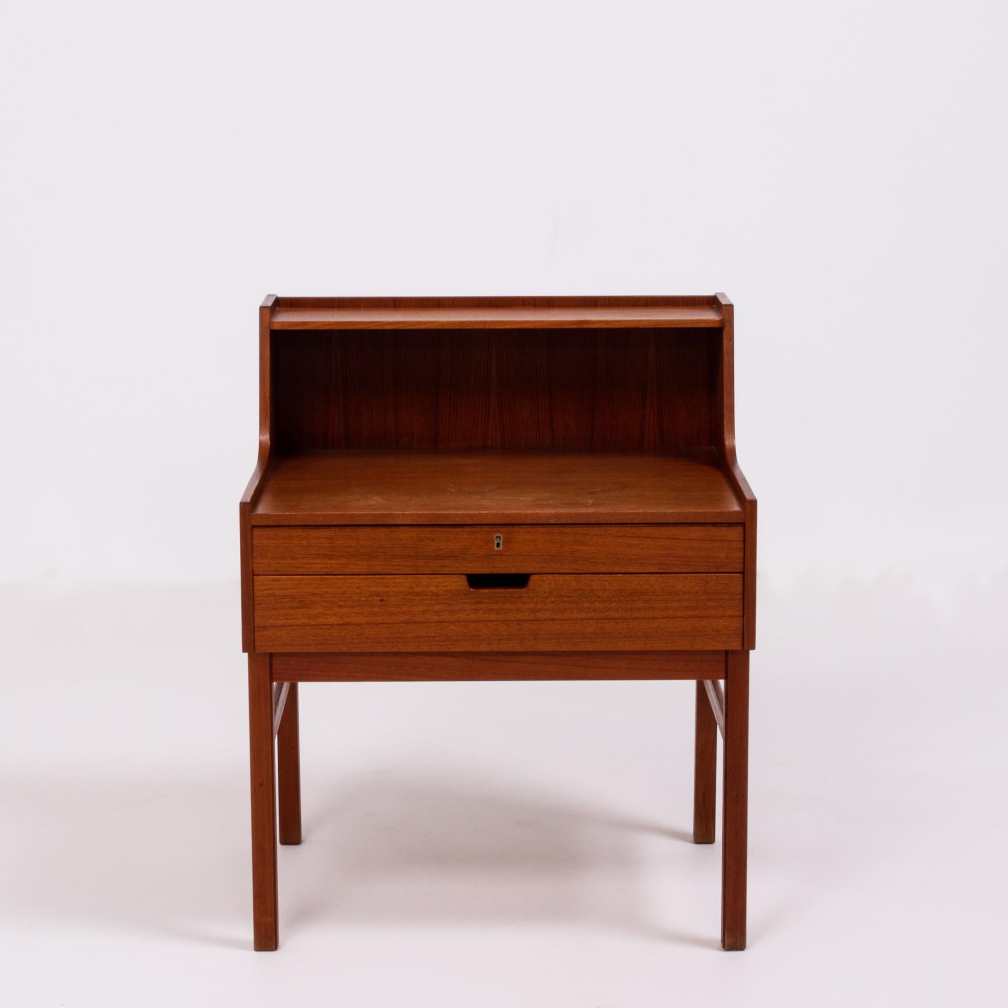 Designed by Sven Engström and Gunnar Myrstrand, this bedside table is beautifully constructed in teak.
Featuring a narrow shelf at the top, the bedside table has two drawers, both with internal dividers. The top drawer can be locked with a key.
  