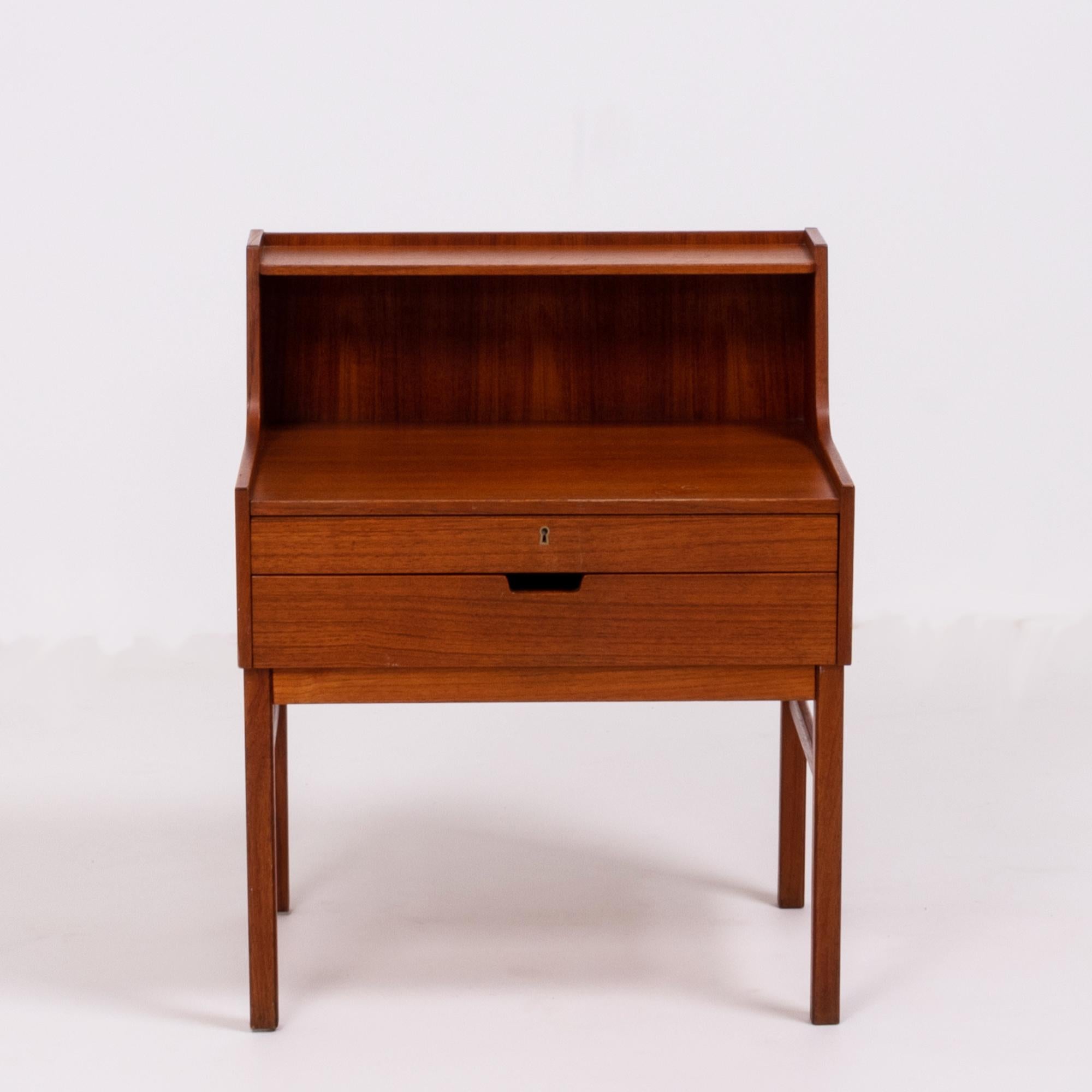 Designed by Sven Engström and Gunnar Myrstrand, this bedside table is beautifully constructed in teak.
Featuring a narrow shelf at the top, the bedside table has two drawers, both with internal dividers. The top drawer can be locked with a key.
   