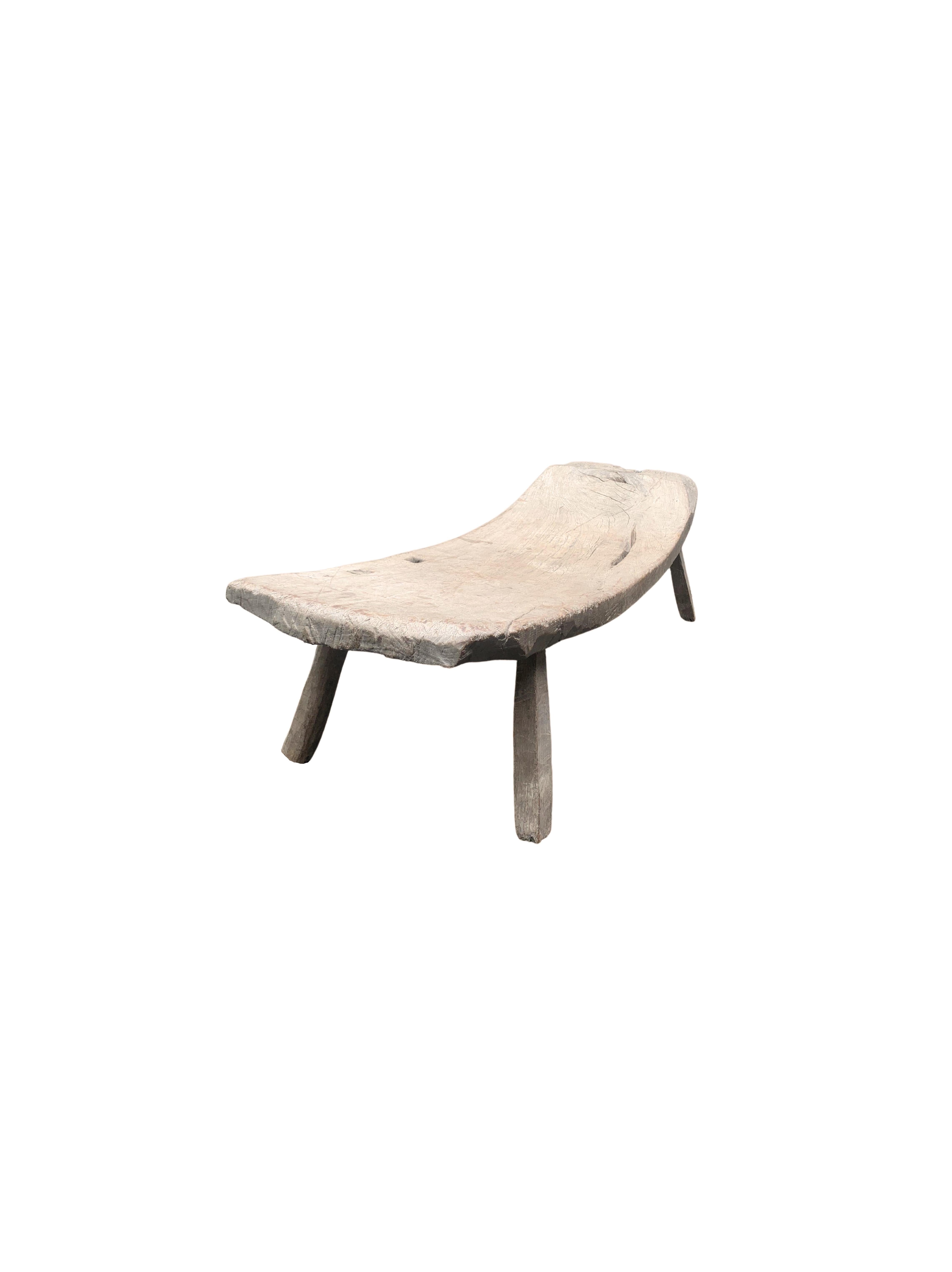 This hand-carved teak wood bench originates from the Island of Madura, off the coast of Northeastern Java. It features a wonderful curved shape with angular legs. The seat was carved from a single block of teak wood and has been given a smooth