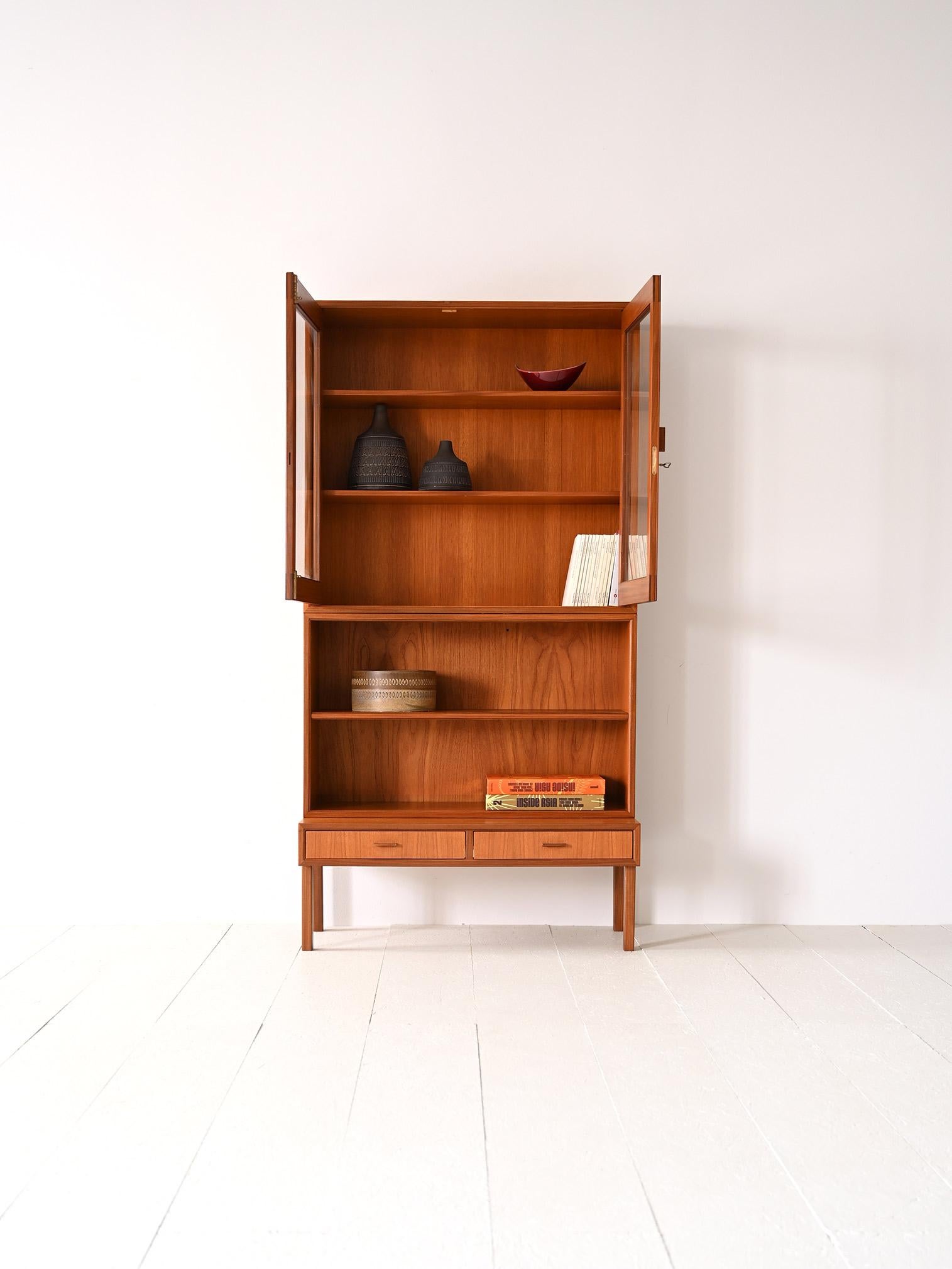Scandinavian 1960s teak cabinet.

A uniquely shaped piece of Swedish modernism.
Consisting of two parts, the lower one is a cabinet with two drawers on which rests a structure formed by shelving and partially closed by two glass doors.
Ideal both as