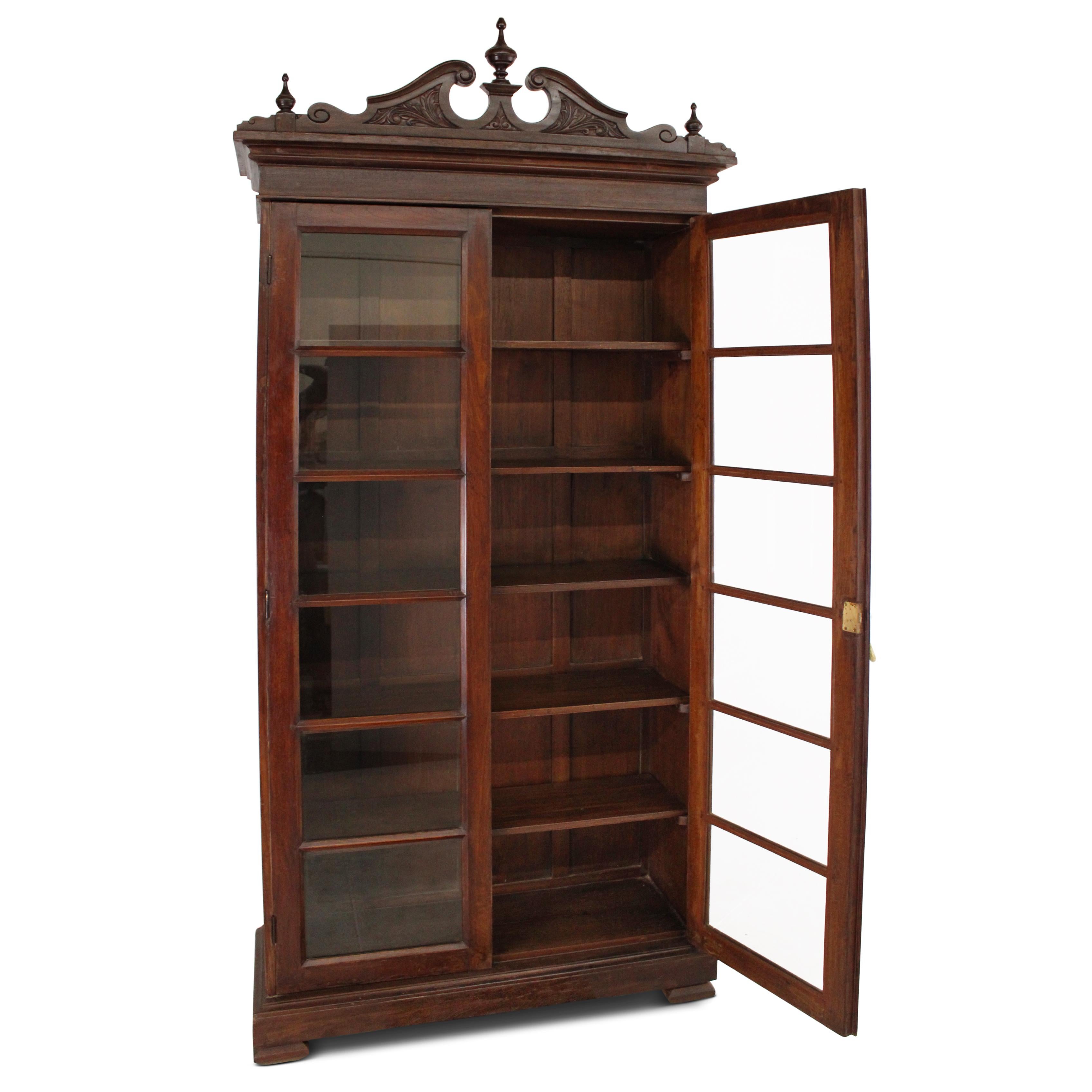 Una magnífica librería de teca de una colección palaciega, con una sólida construcción y estanterías. Esta librería está realzada con paneles de puerta acristalados y una tapa de corona bellamente tallada. Está en excelentes condiciones y dispone de