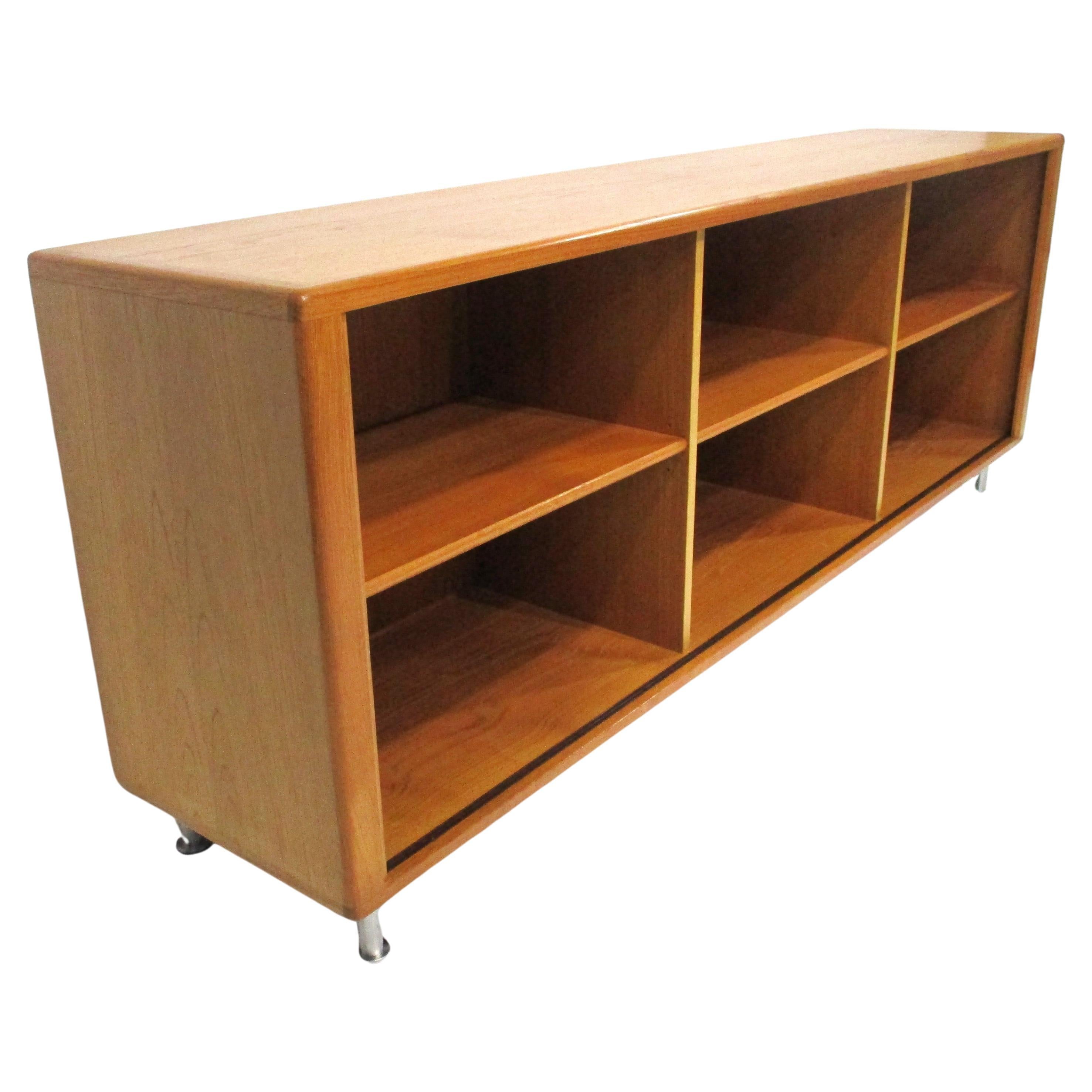 A medium toned teak wood bookcase with adjustable shelves sitting on brushed aluminum legs . Three sections with one shelve each gives you plenty of storage for books or vinyl records with legs that are adjustable and have pads to protect your