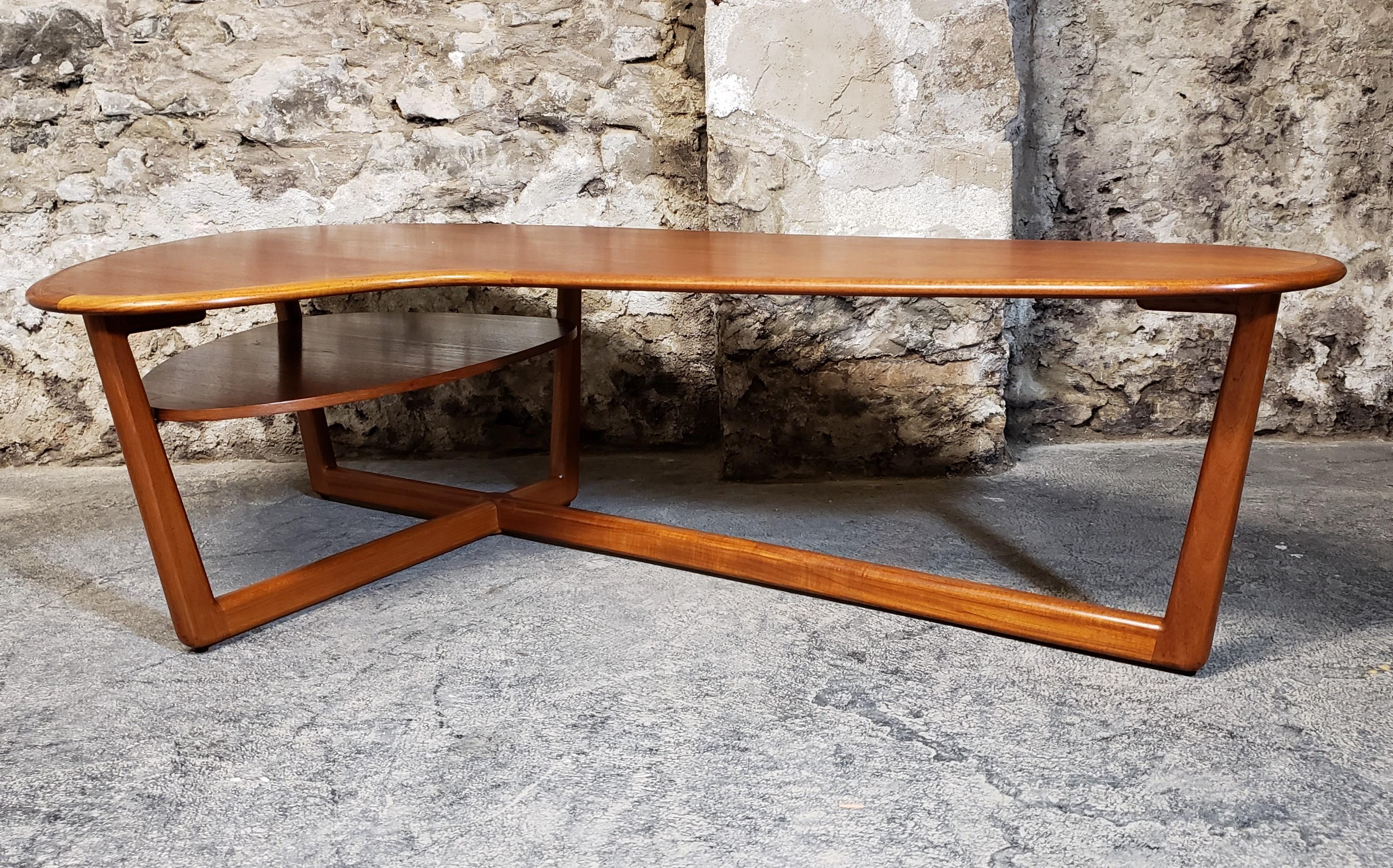 Gorgeously sculpted teak boomerang coffee table. Mid-Century Modern take on this classic design shape. It features a beautiful rich patina from aged teak wood, rounded solid teak edges and a floating magazine rack or shelf underneath. The
