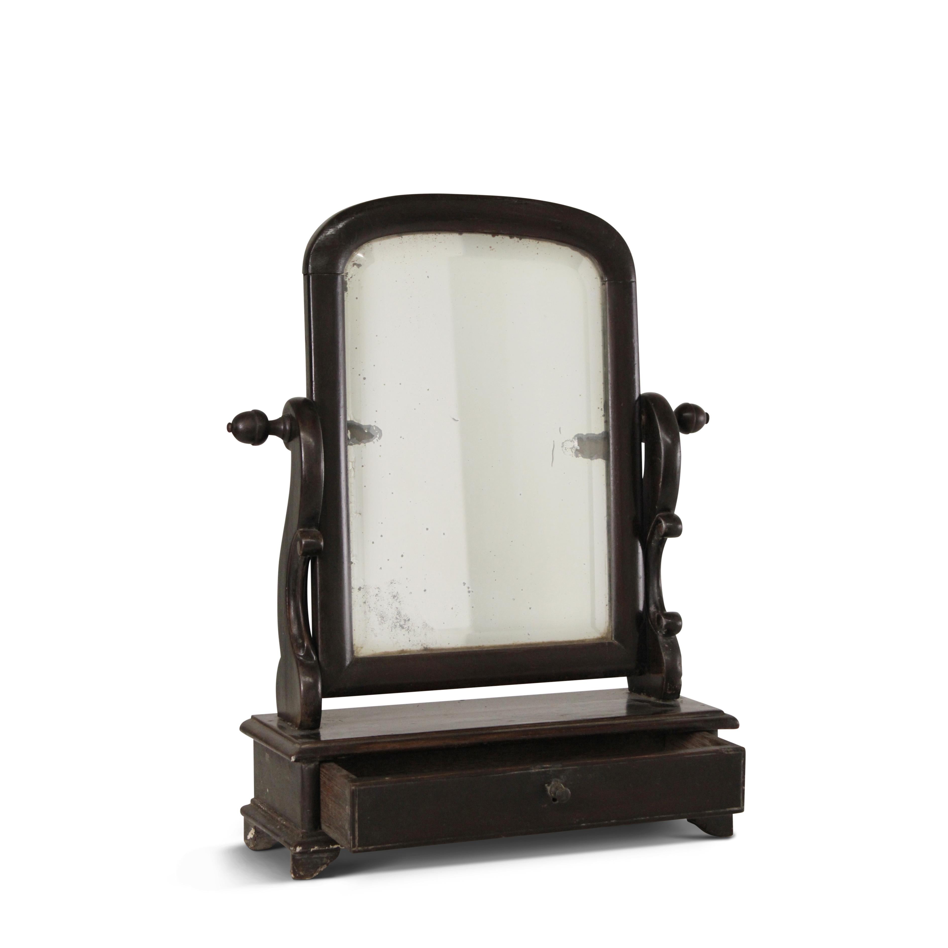 A charming teak tabletop vanity mirror with scrolled side supports, original arched top mirror frame and a drawer at the bottom. The mirror surface reveals the passage of time with a graceful patina.