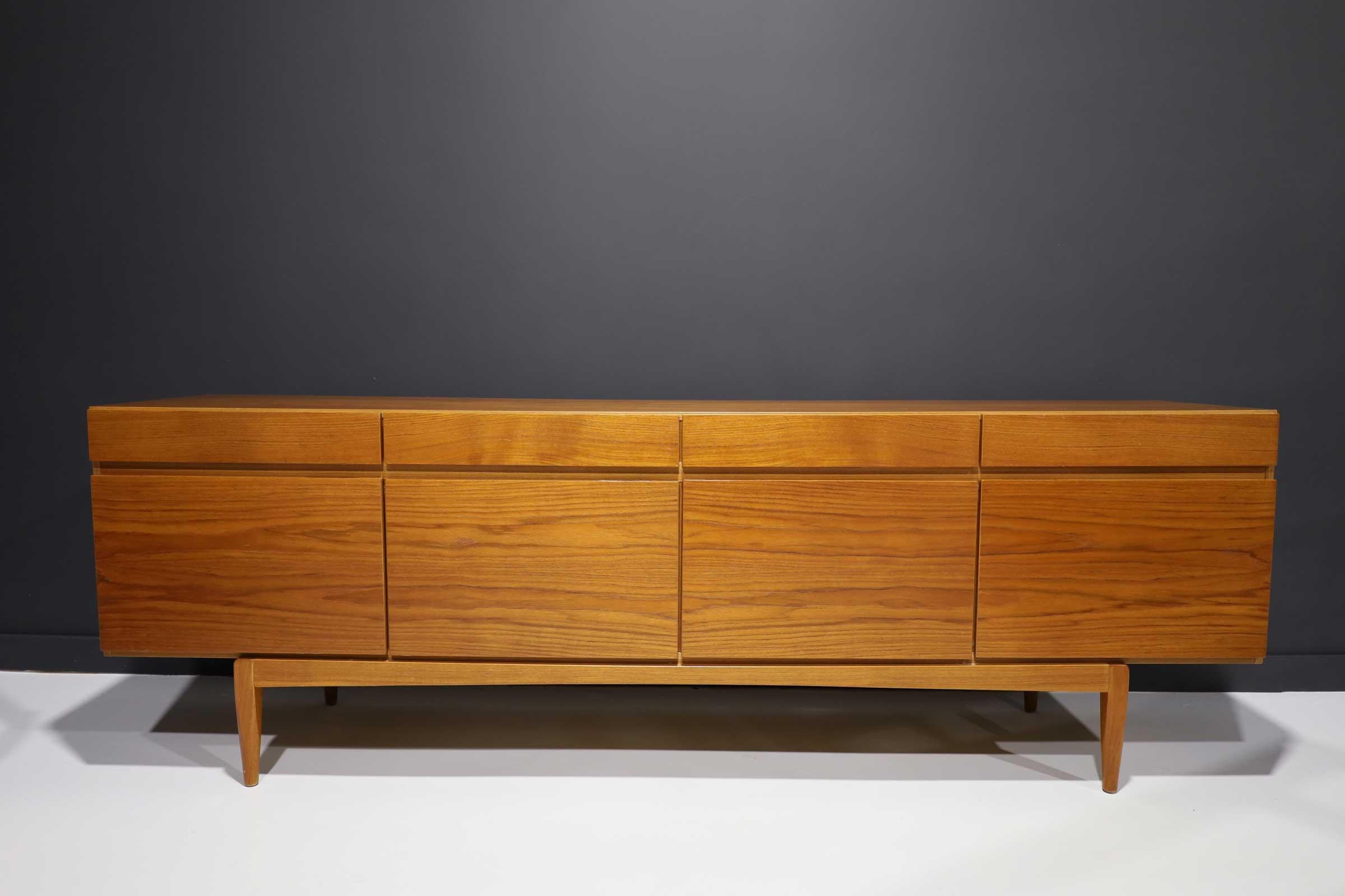 This stately teak sideboard, model 66, by Ib Kofod-Larsen is solidly constructed, with minimal, clean lines. Set on a raised base, the case provides ample storage. Four roomy drawers are aligned above four doors; five felt-lined cutlery drawers