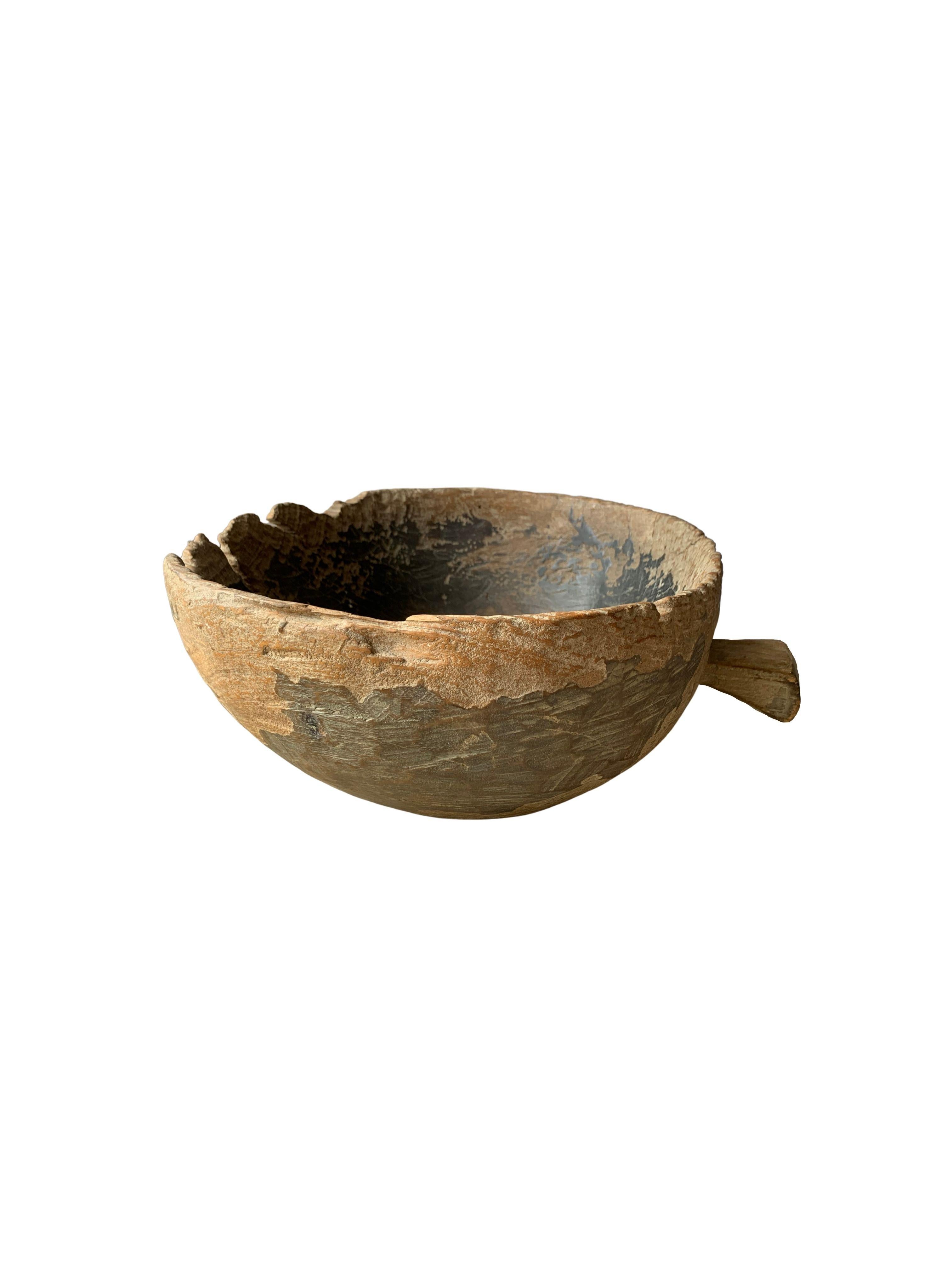 A teak burl wood bowl crafted on the island of Java, Indonesia. The bowl was cut from a much larger slab of burl wood and maintains an organic shape and natural texture. It has aged considerably over the decades contributing to its appeal. 

