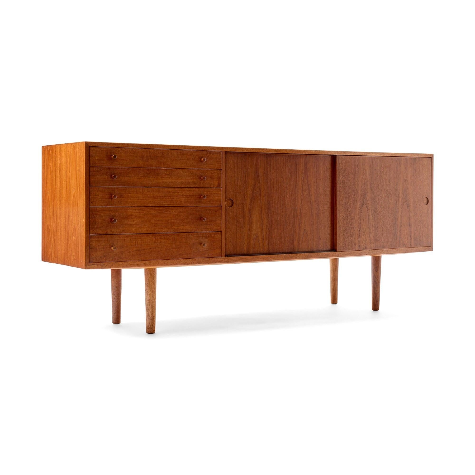 Credenza in teak caldo con una serie di cinque cassetti e due scomparti con ante scorrevoli e ripiani regolabili, che poggiano su gambe a tasselli in teak massiccio tornite.
