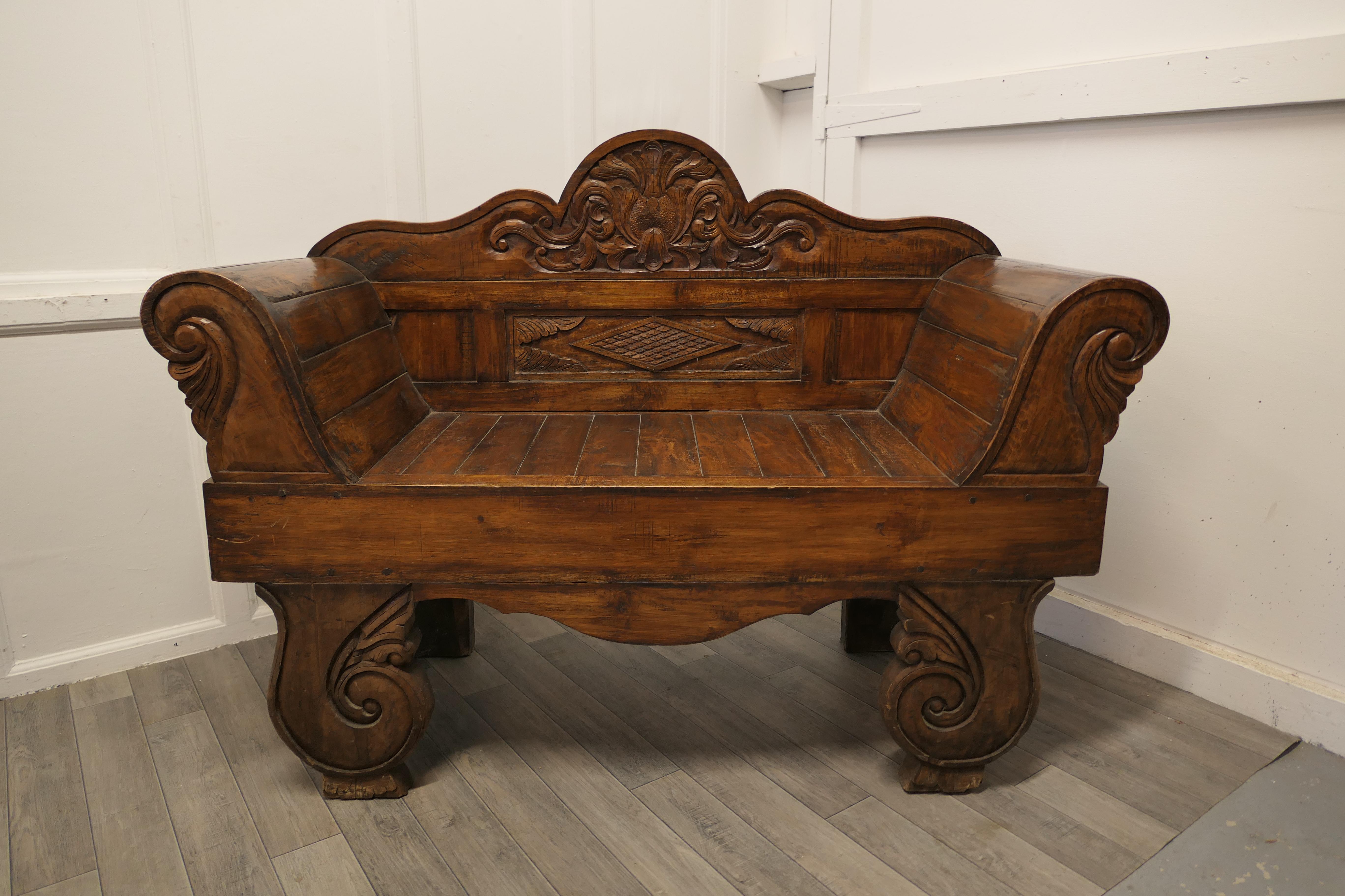 Teak carved settee, bench

This is a sturdy piece, the settee or bench has a carved curved high back with more carving on the front of the arms and legs
The bench is in good all round condition and has an outward curved shape with broad arm rests
