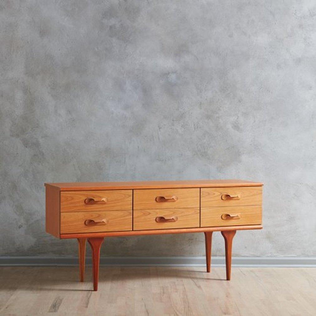 A 1960s chest of drawers by AustinSuite constructed with beautifully grained teak wood. This sleek chest features clean, Danish inspired lines and has six drawers with sculptural carved pulls. It stands on four tapered legs and retains an
