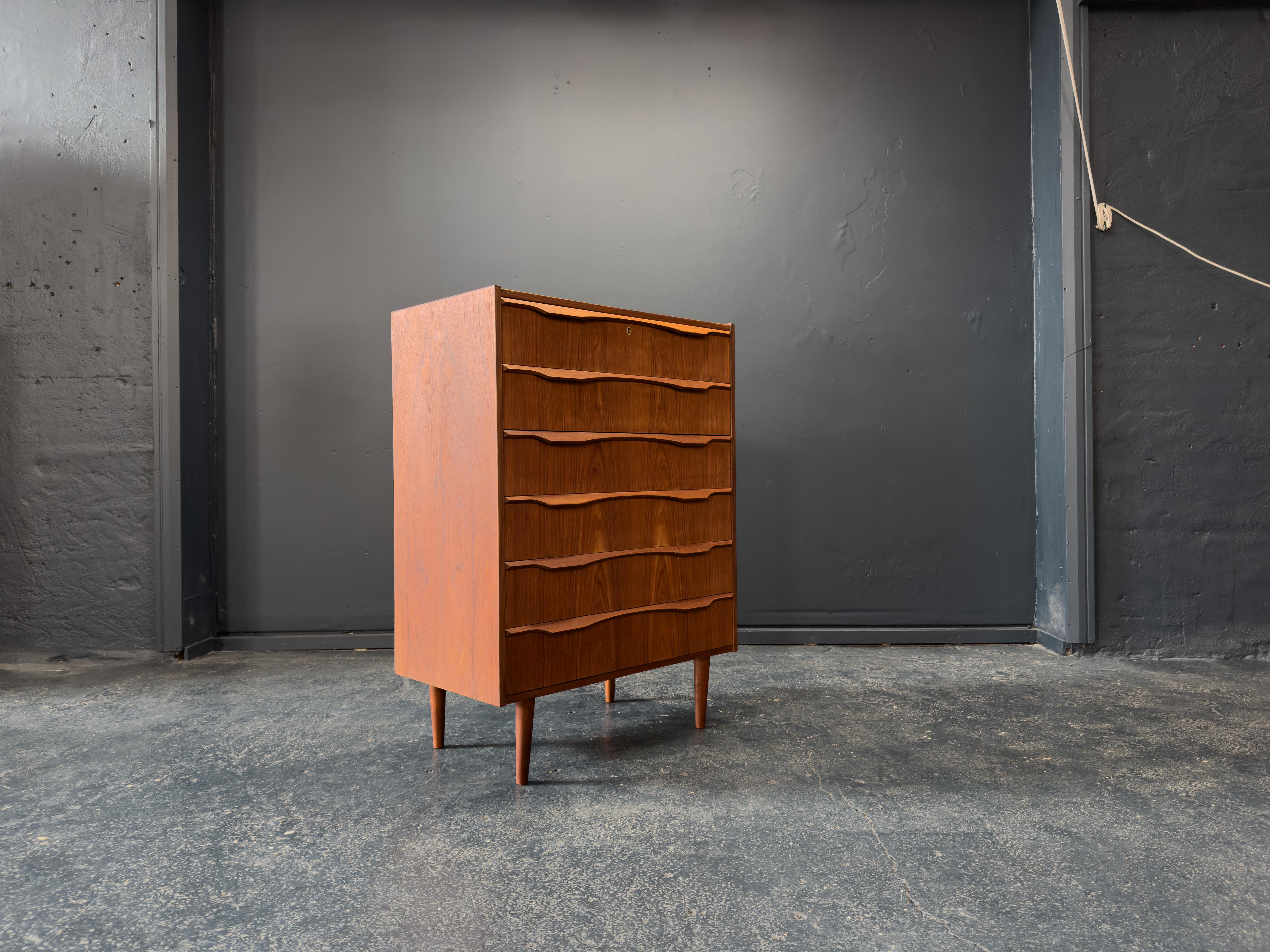 This beautifully crafted mid-century modern chest of drawers features a striking sculptural front and elegant simplicity characteristic of Scandinavian design. Made from richly grained teak, the piece showcases a warm, natural finish and superb