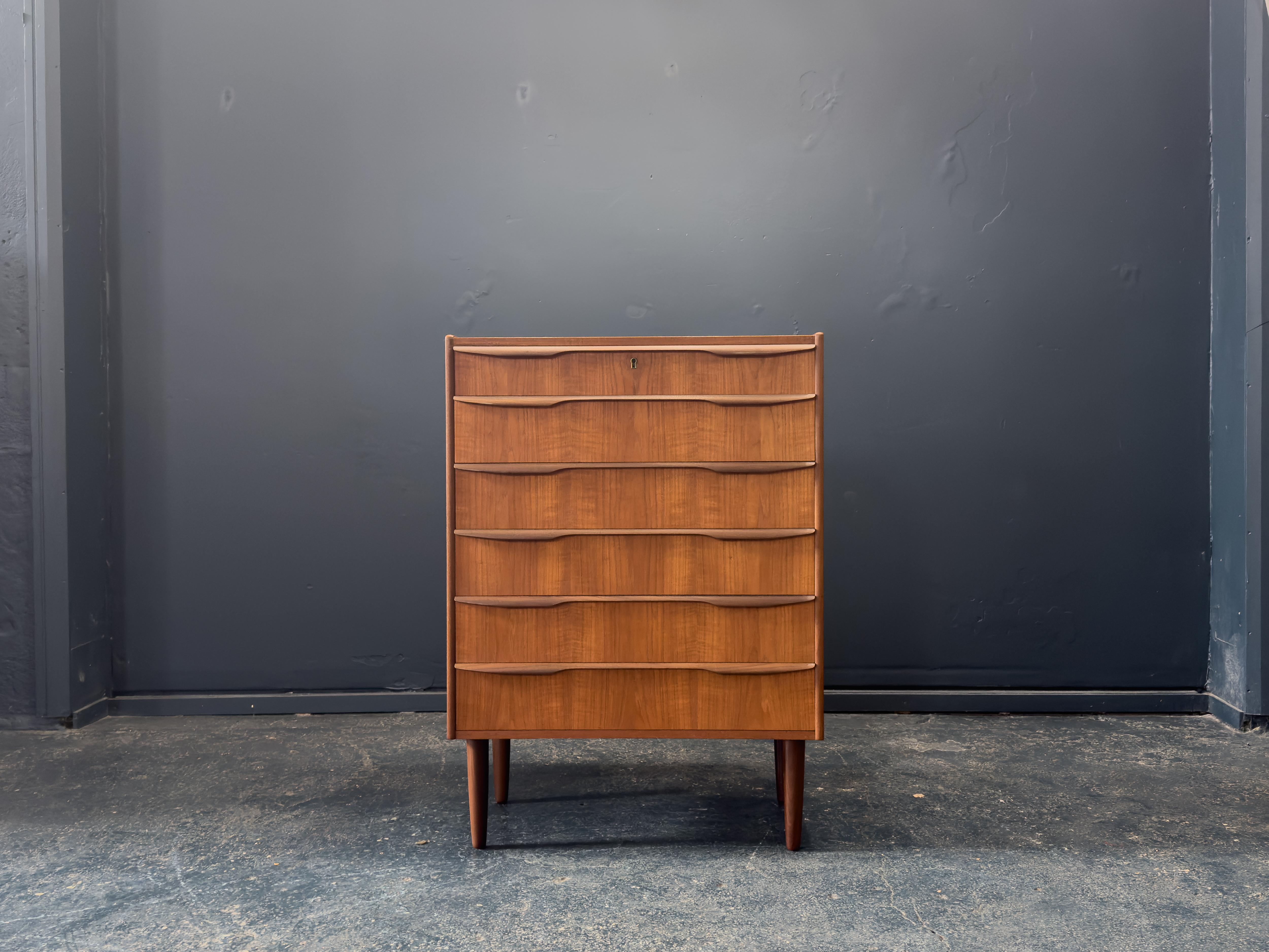 Questa straordinaria cassettiera in teak è un raffinato esempio di design scandinavo di metà secolo, che si distingue per le proporzioni eleganti e i frontali scultorei dei cassetti. La silhouette alta e stretta offre una generosa quantità di spazio