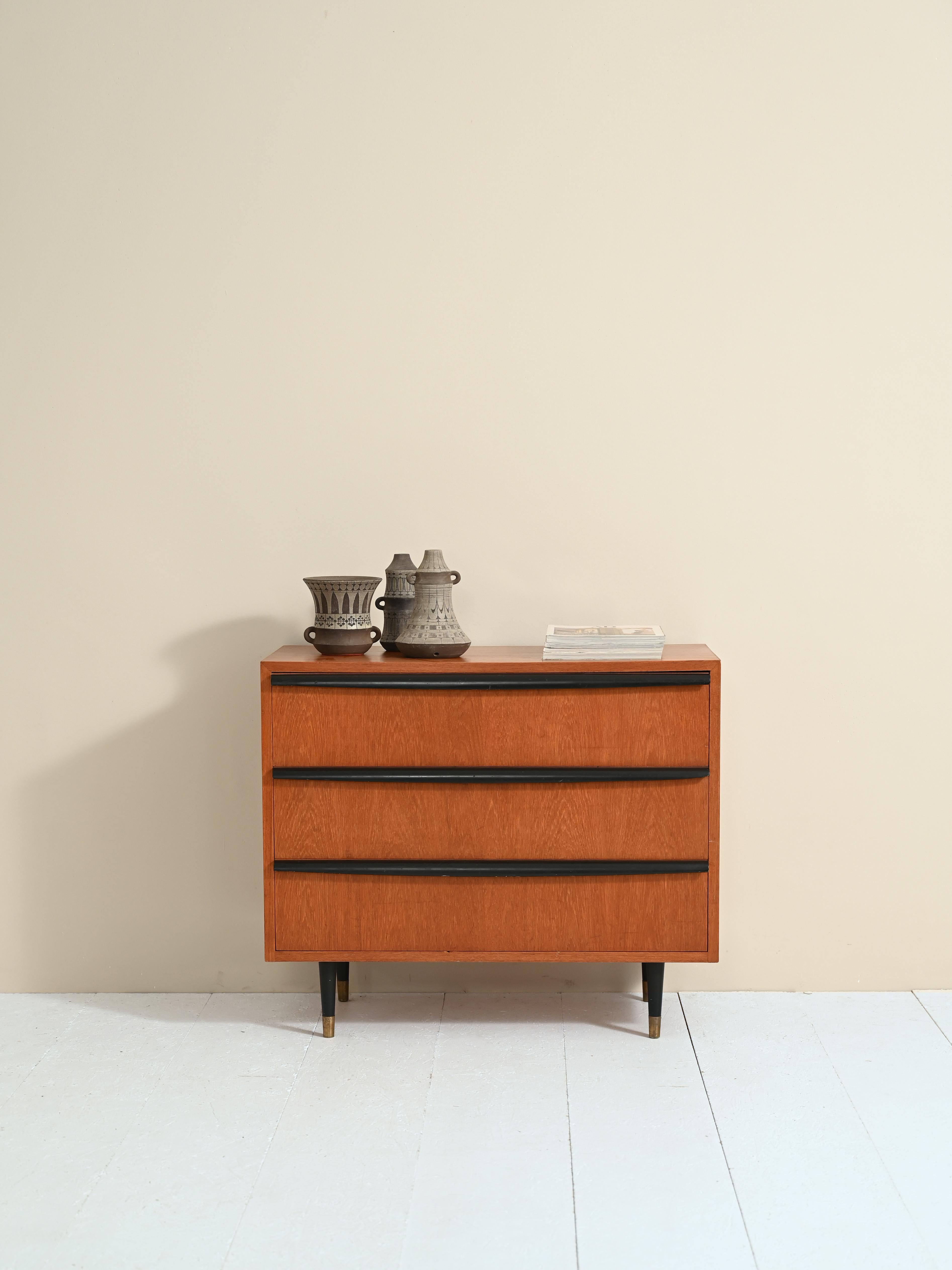 Original Scandinavian cabinet with three drawers and brass finials.

The special feature of this cabinet is undoubtedly the handle of the drawers formed by carved wooden slats 70 centimeters long and painted black like the legs.
The lower part