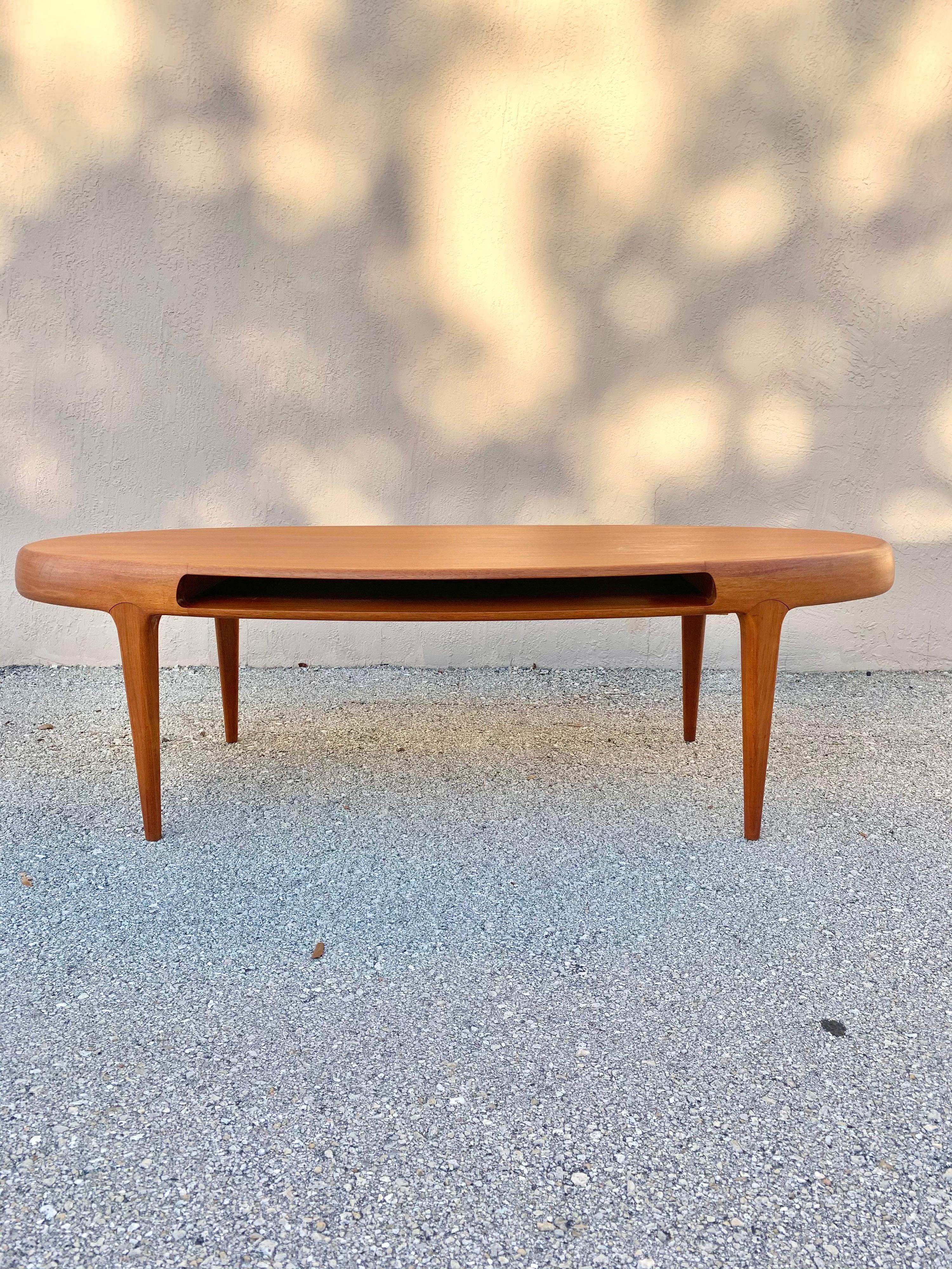 Teak coffee table designed by Johannes Andersen. A testament in Danish Mid Century Modern design. Gorgeous thick rails of solid teak surround the table top. Legs fit seamlessly into the table. Table has a magazine rack that goes all the way through