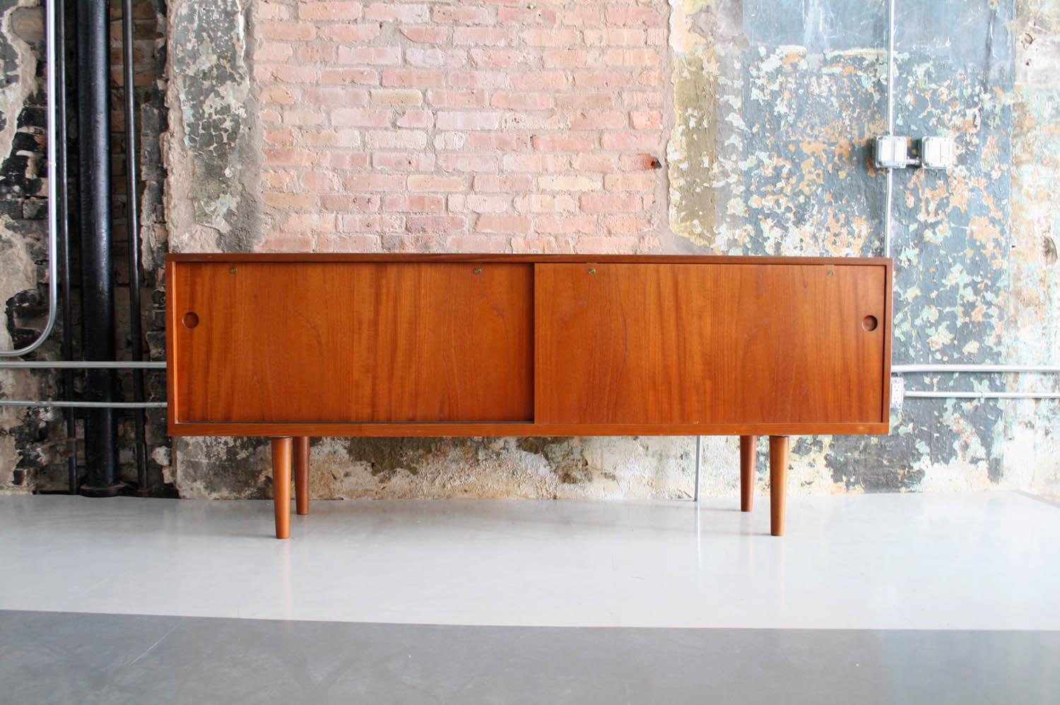 This credenza is a model 26, in oak, teak and brass, designed by Hans Wegner and produced in Denmark by Ry Mobler. The credenza features sliding doors that open to show a series of storage spaces, adjustable shelves, and drawers. The interior is