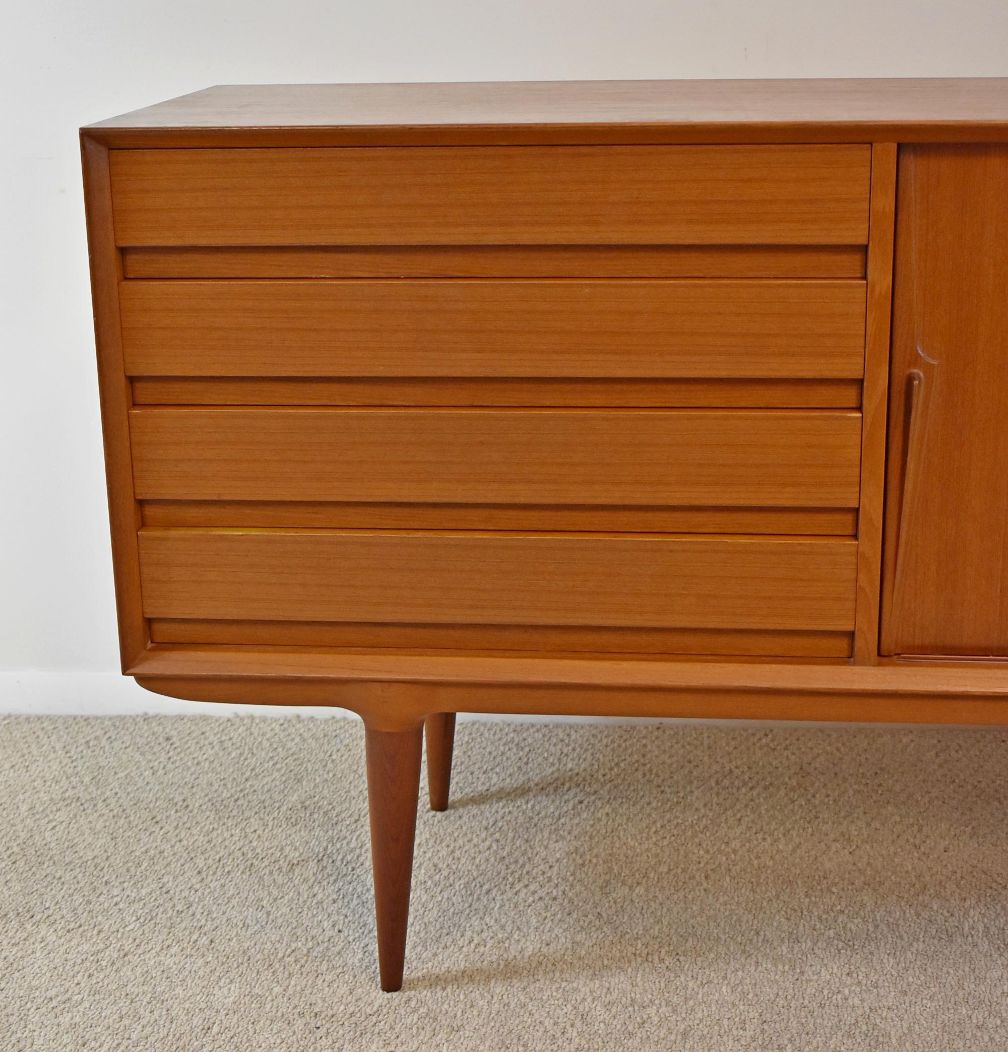 Teak Credenza. Circa 1958. Four drawers and two sliding doors. Model NR18 by Omann Jun Mobelfabrik (Danish, established 1933). Felted tray within one drawer. Good Vintage condition, disconnected from base/feet, some light surface wear consistent