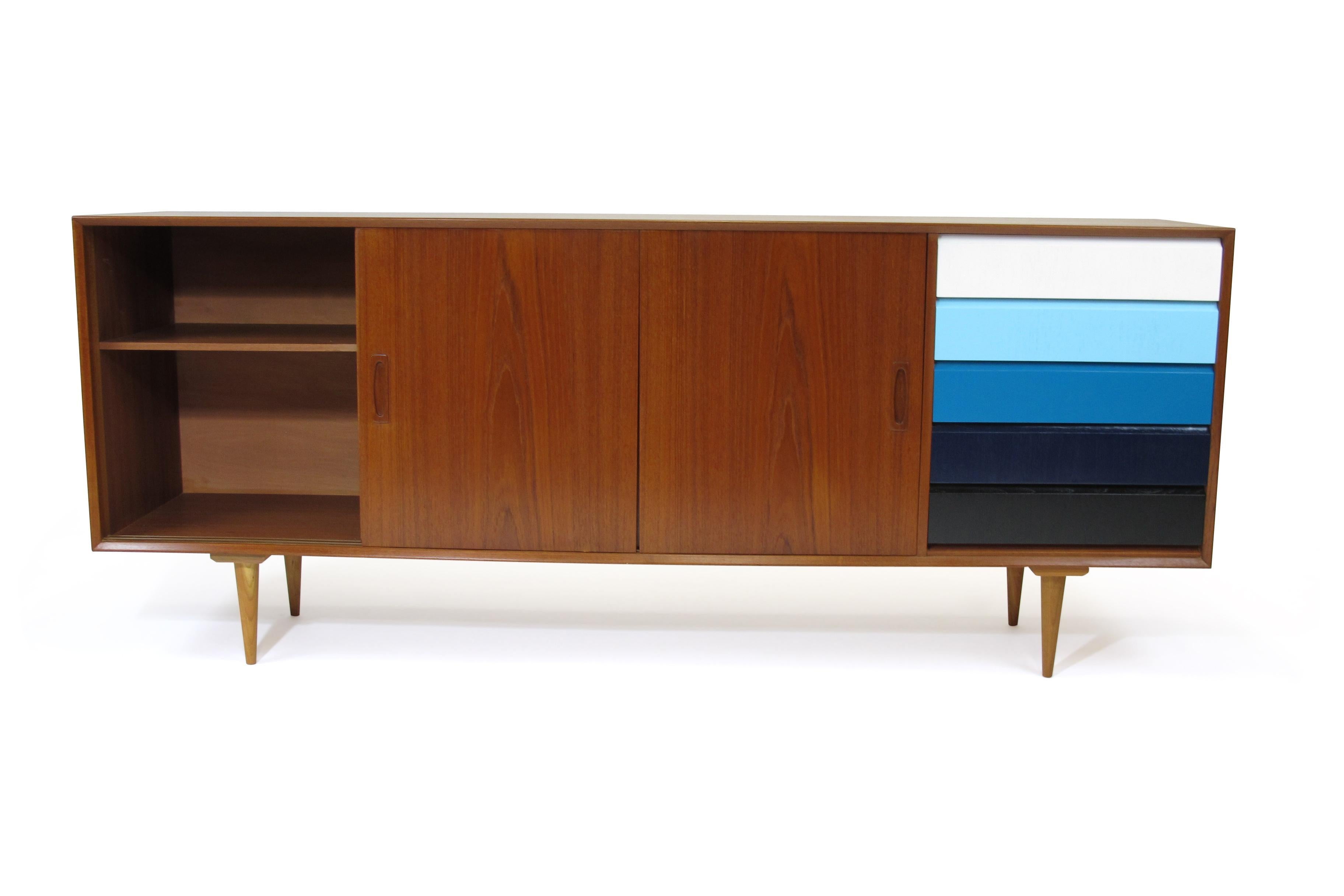 Danish teak credenza with sliding doors and adjustable interior shelf, series of color blocked drawers on right. Raised on tapered wood legs.