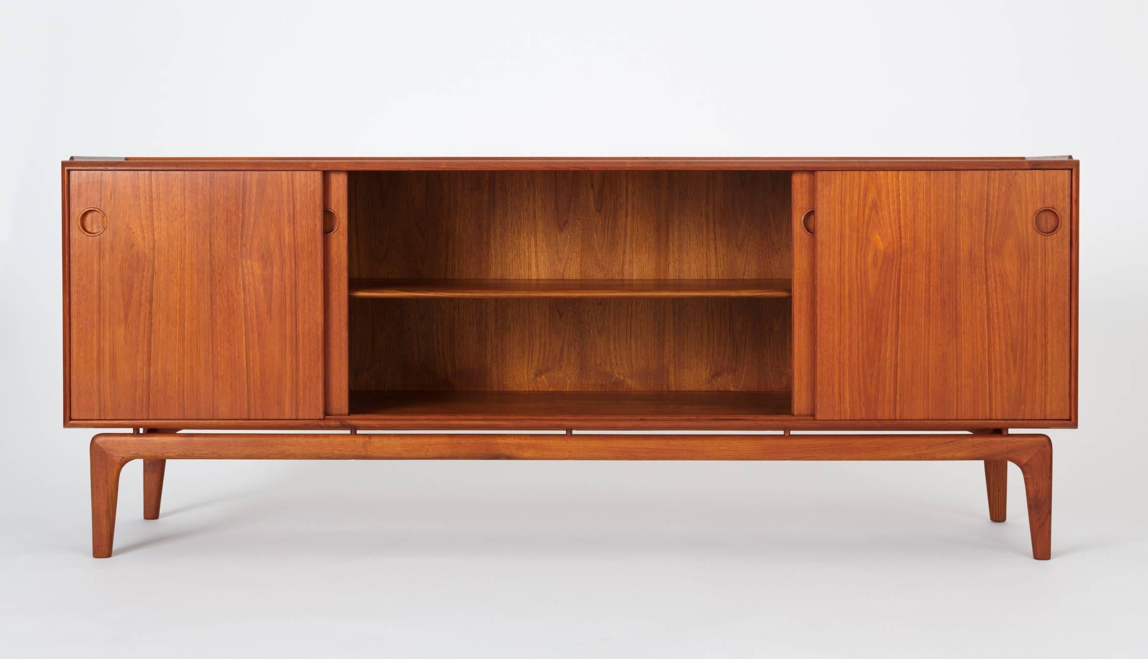 A Danish modern teak credenza or sideboard from Arne Hovmand Olsen for Mogens Kold Møbelfabrik. The piece has four sliding panel doors on two sets of runners, allowing flexibility of access or display. Each door opens at a recessed round pull. The