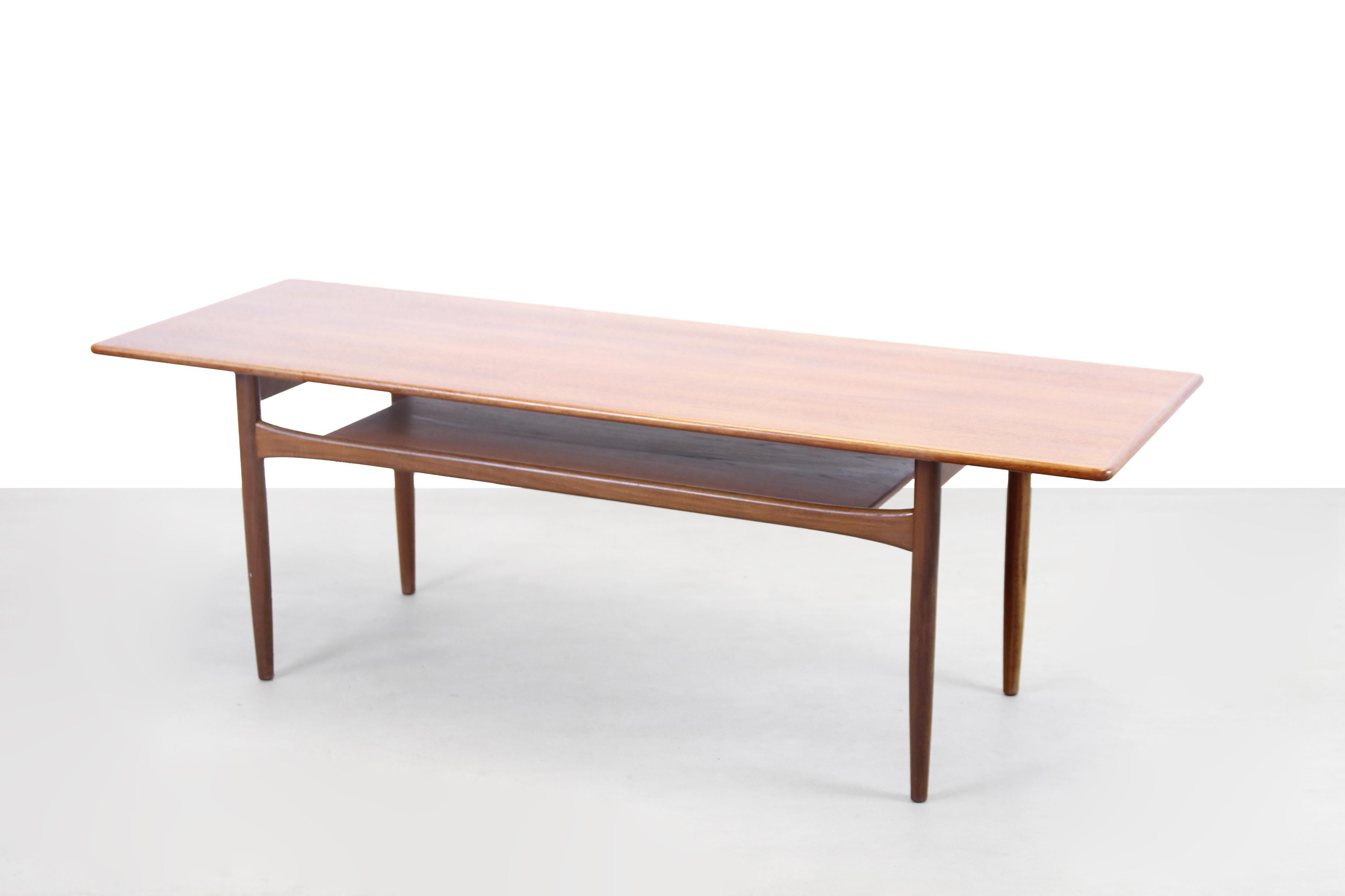 Beautiful vintage coffee table from Denmark with a teak shelf for storing magazines or, for example, the remote control. Made of teak veneer and solid teak. The coffee table is 153 cm long, 53 cm deep and has a height of 51 cm. The height can be