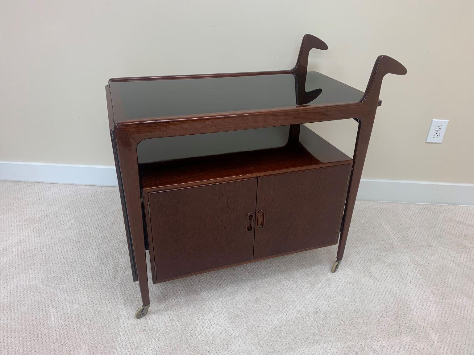 Professionally restored Danish modern bar cart possibly by Falster in a gloss finish. This unique example has a drop down top, which when extended creates a large serving area. Lower section has two doors for great storage. Height to top of serving