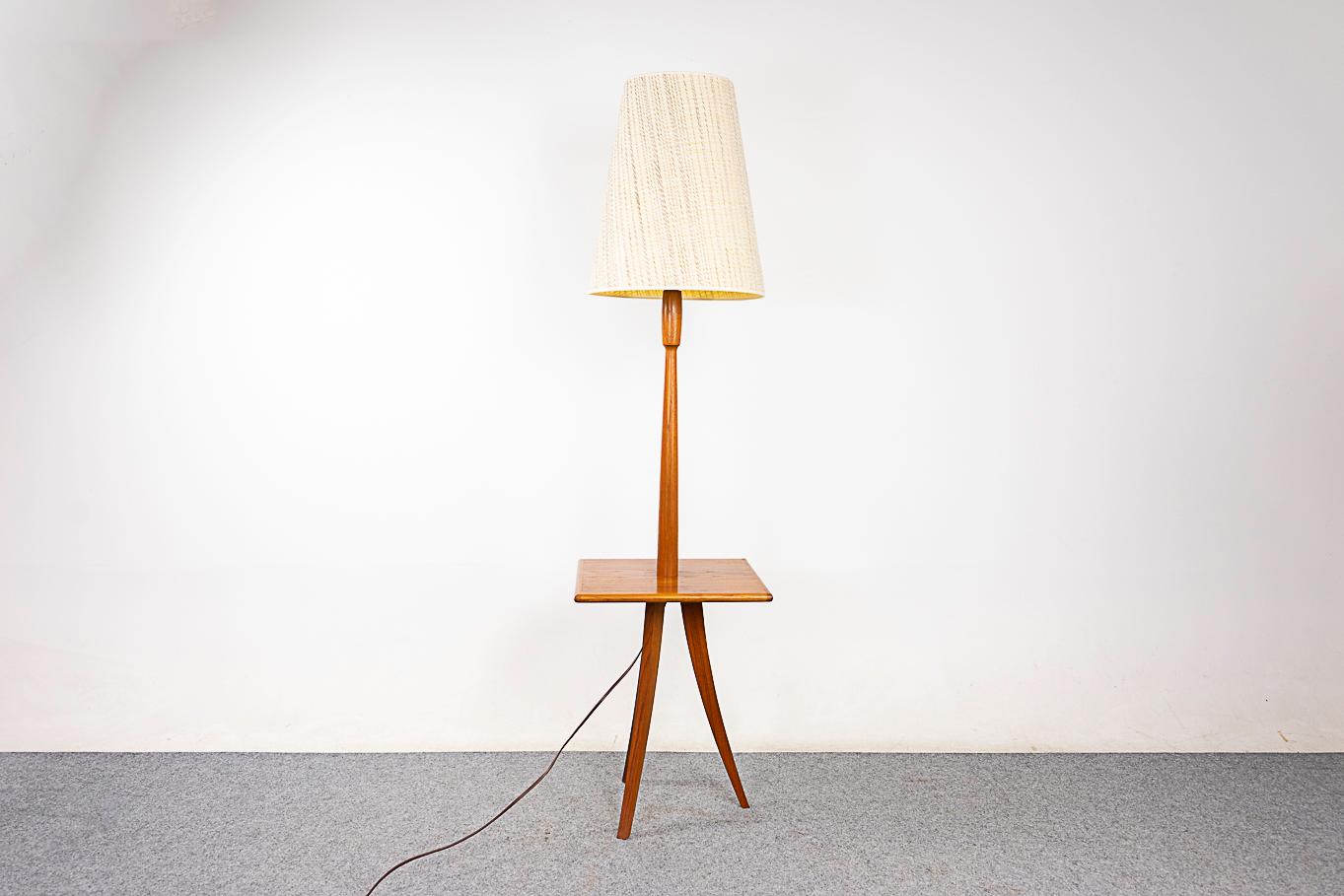 Teak mid-century floor lamp, circa 1960's. Handy built in table with beveled edges and stunning wood graining. Sultry curved legs on this rare tripod design! Lovely bullet shaped detail at the top of the neck. Tri-light socket allows 3 brightness