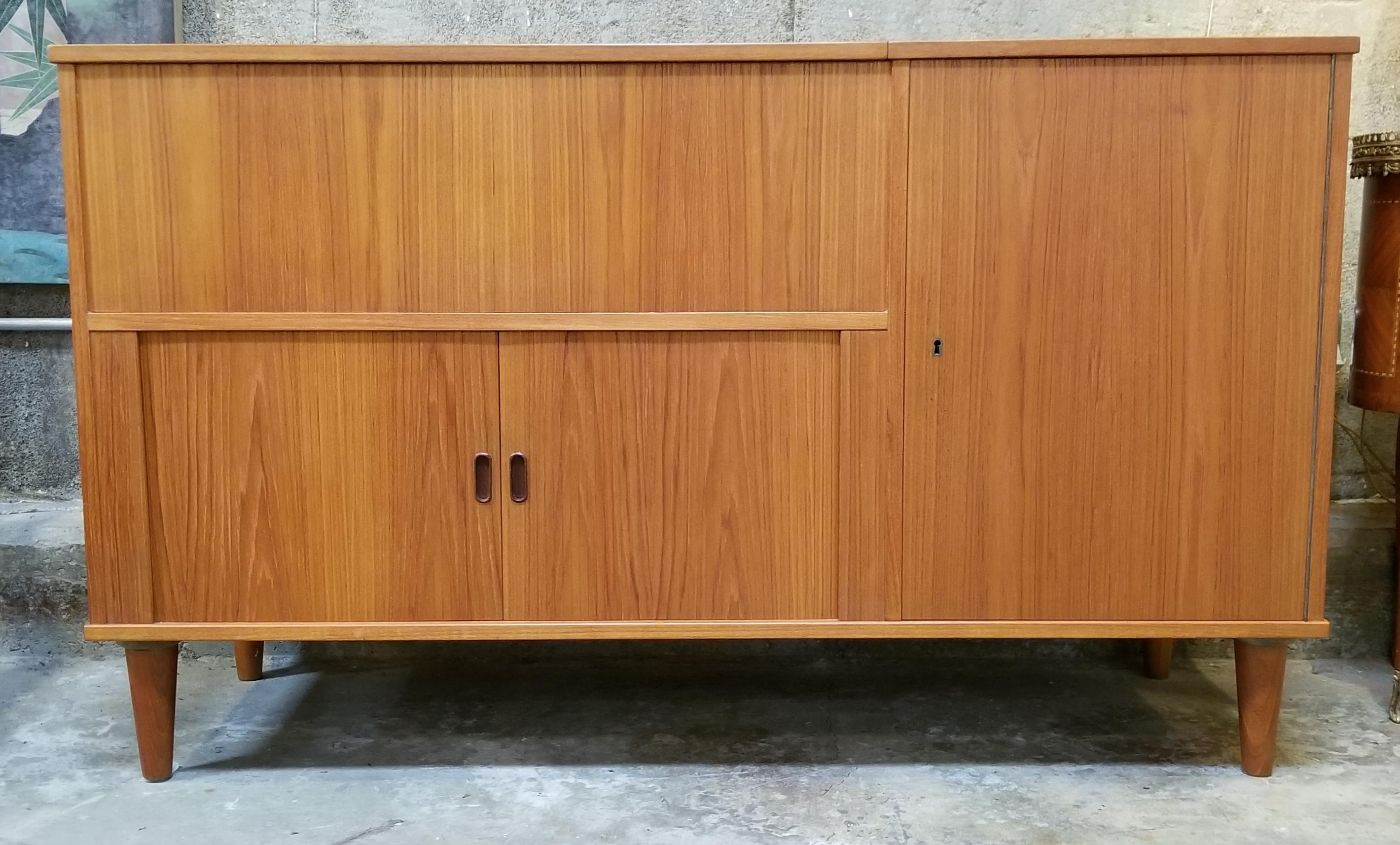 A 1960s teak Danish Modern stereo cabinet featuring a lift-up top, tambour doors and a locking cabinet with shelf. In exceptional original vintage condition with original finish. Classic peg leg detail. In the manner of Arne Vodder.
