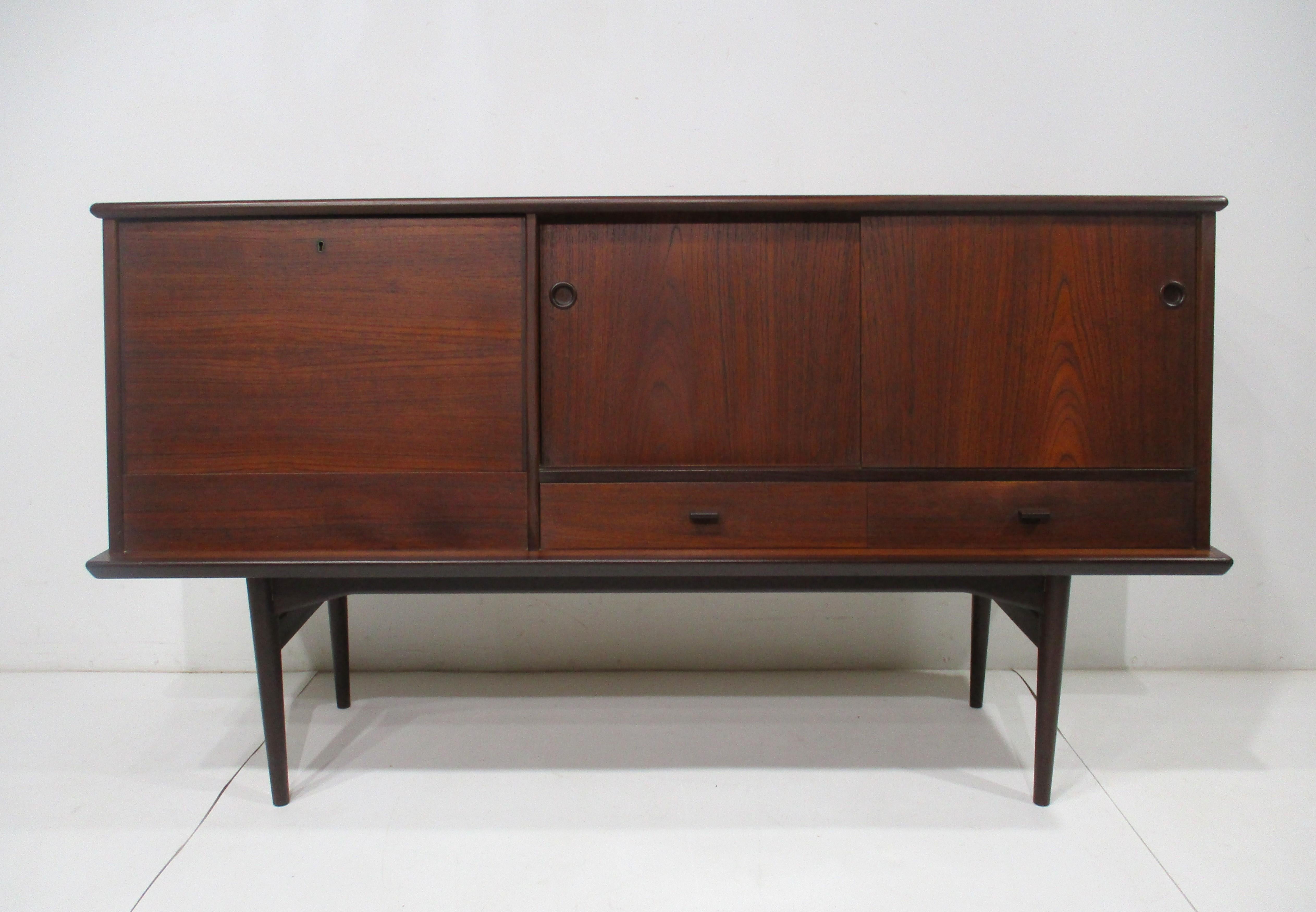 A very well made Danish modern styled credenza bar cabinet with locking pull down door having a Laminate surface with automatic light and mirrored back . The other side has two sliding doors with a contrasting birch storage area , two adjustable
