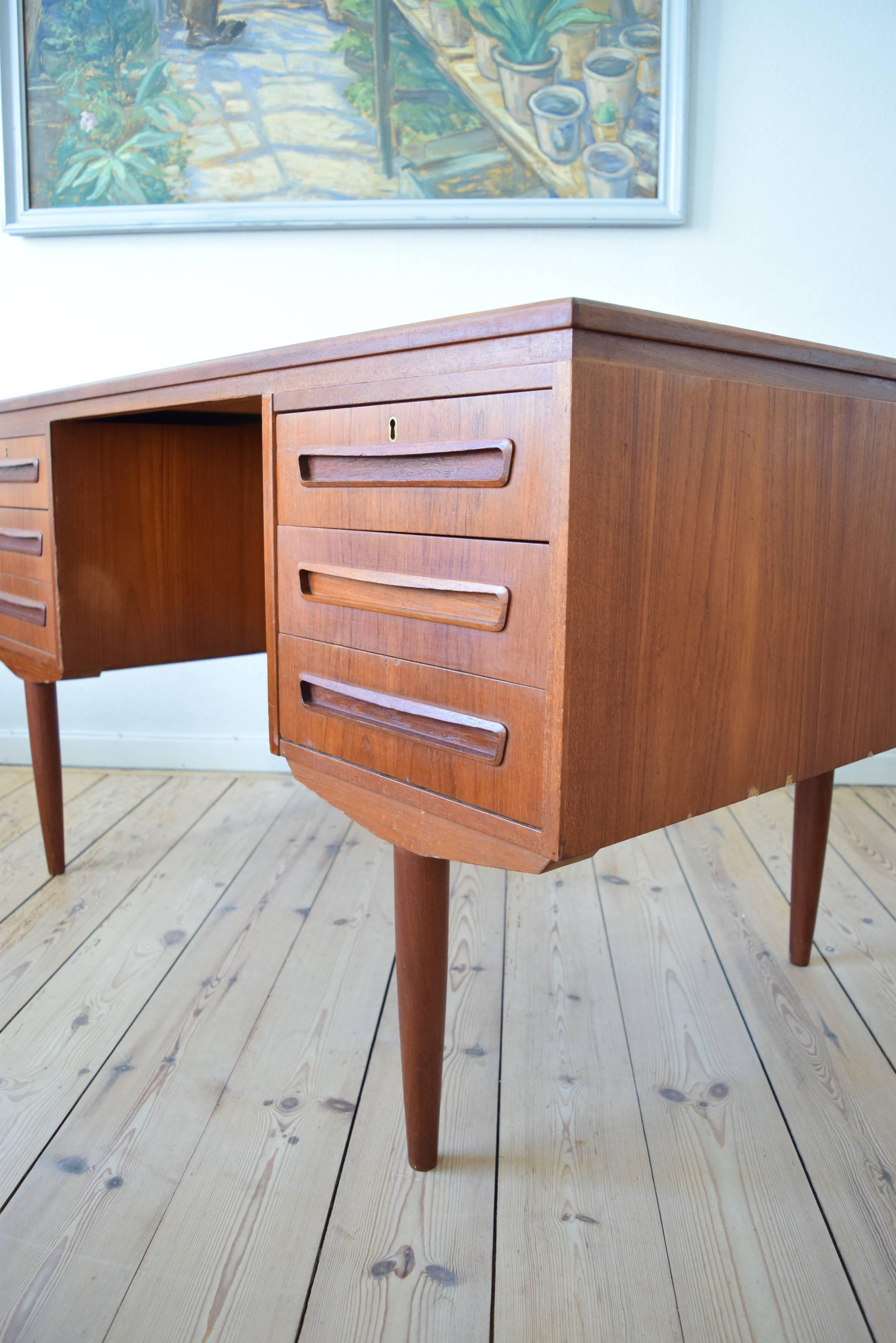 Teak desk designed by J. Svenstrup for A.P. Møbler, Denmark in the 1960s. Desk features six drawers (two lockable) on the front, and bar cabinet on the back side. Sits on turned and tapered solid teak legs. Apart from some marks on the top plate