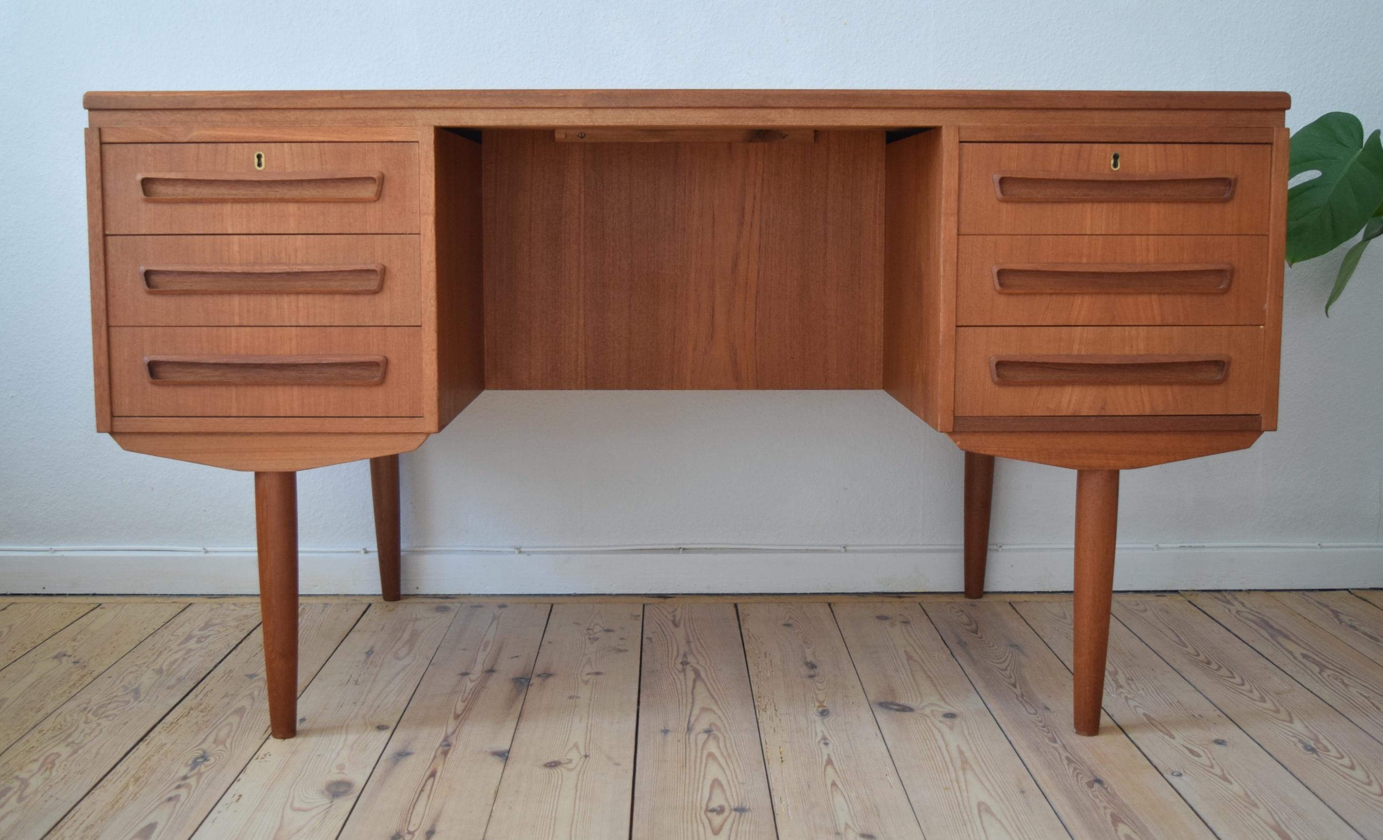 Teak desk designed by J. Svenstrup for A.P. Møbler, Denmark in the 1960s. Desk features six drawers (two lockable) on the front, and bar cabinet or bookshelves on the back side. Sits on turned and tapered teak legs. Some small marks here and there