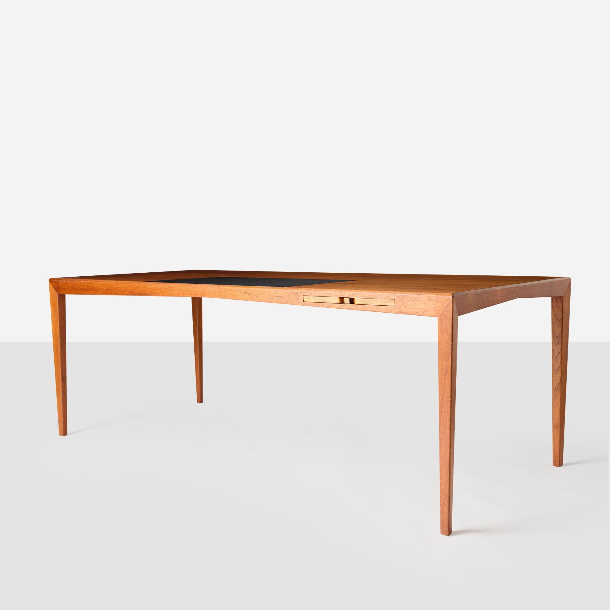 Un bureau en teck, doté d'un pad en cuir et d'un élégant tiroir intégré pour un rangement pratique. Portant la marque du fabricant Åtvidabergs Snickerifabrik sur le tiroir intérieur, cette pièce reflète la qualité et le savoir-faire du design