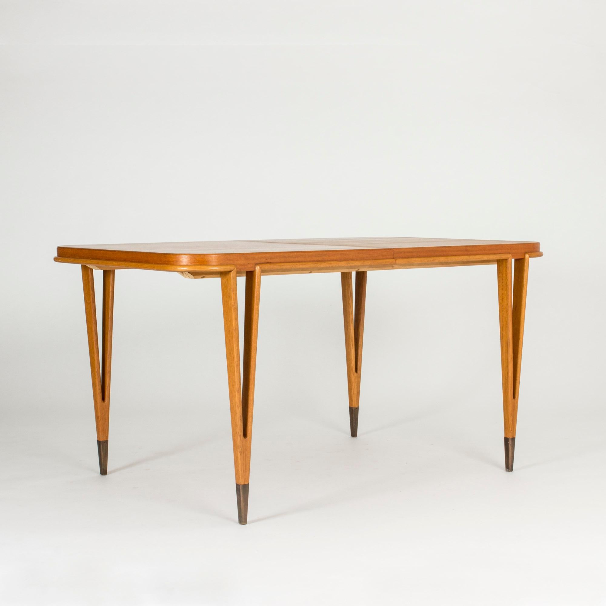 Striking, rare dining table by Bertil Fridhagen with amazing sharply V-shaped legs that form open shapes. A rim that joins the legs runs around the edge of the table top. Two extra leaves. Made from teak with brass feet.

The width of the table is