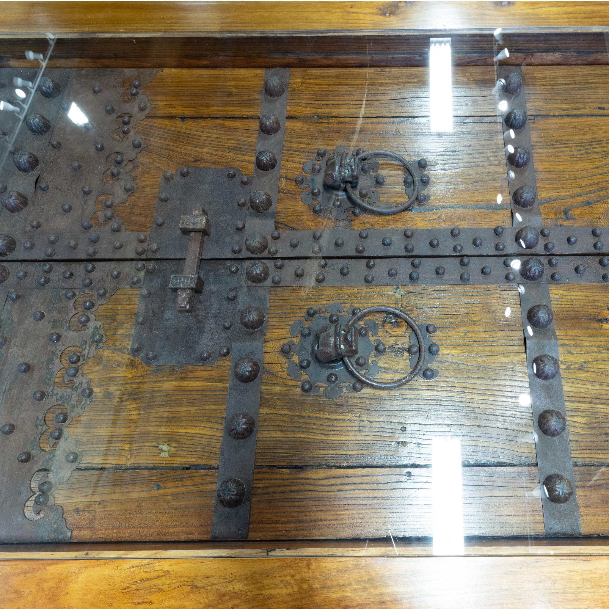 Teak door table made in Australia and shipped to Coeur d'Alene by a doctor. Teak frame and post legs with inset vintage heavily iron decorated teak door. Glass top. Beautiful and unusual table-statement piece that would complement a rustic dining