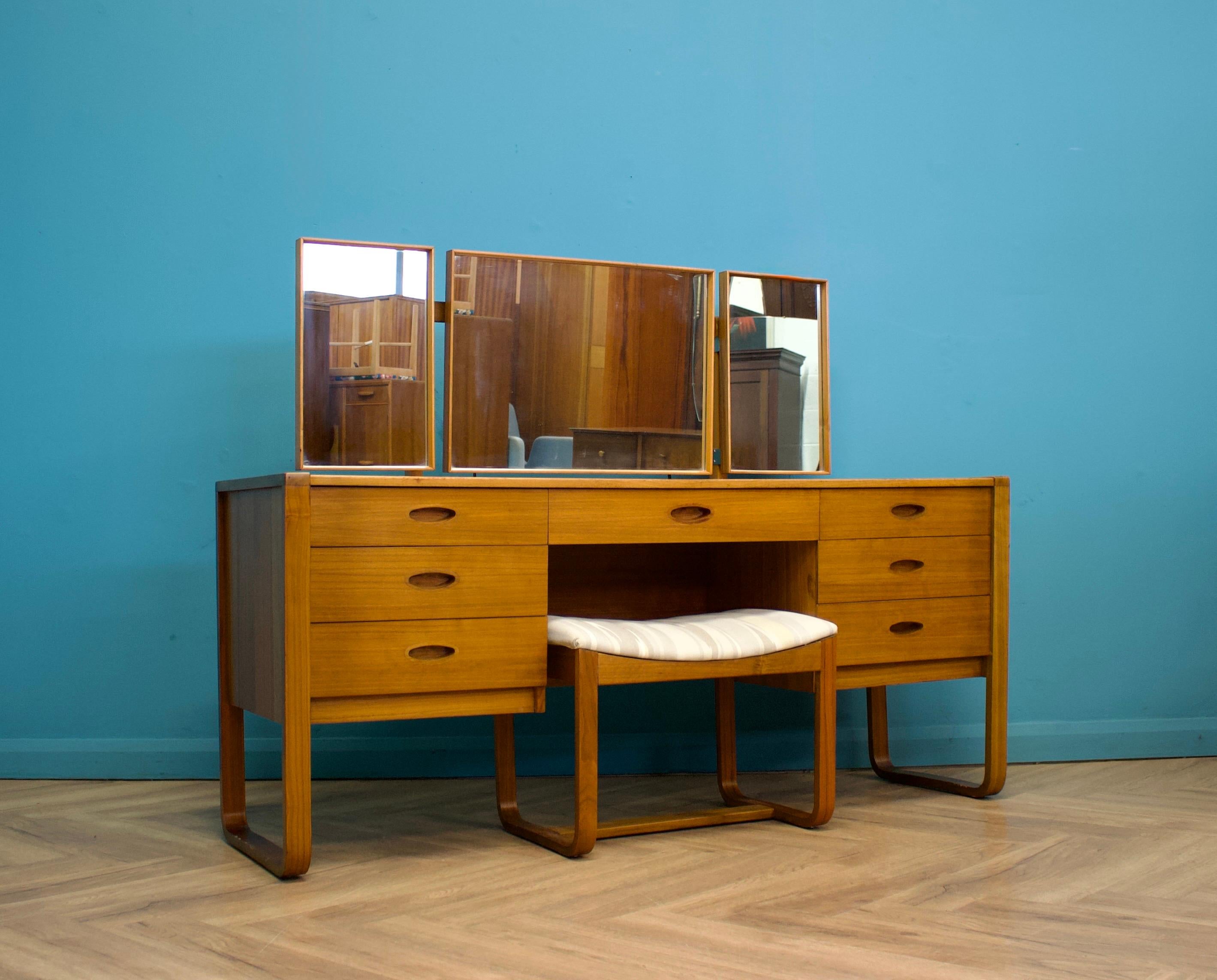 A mid century teak dressing table from Uniflex, circa 1960s

There's a triptych mirror, the middle tilts, the two sides swivel

Featuring seven drawers each with an oval recessed handle

The stool would benefit from being recovered

Height to the