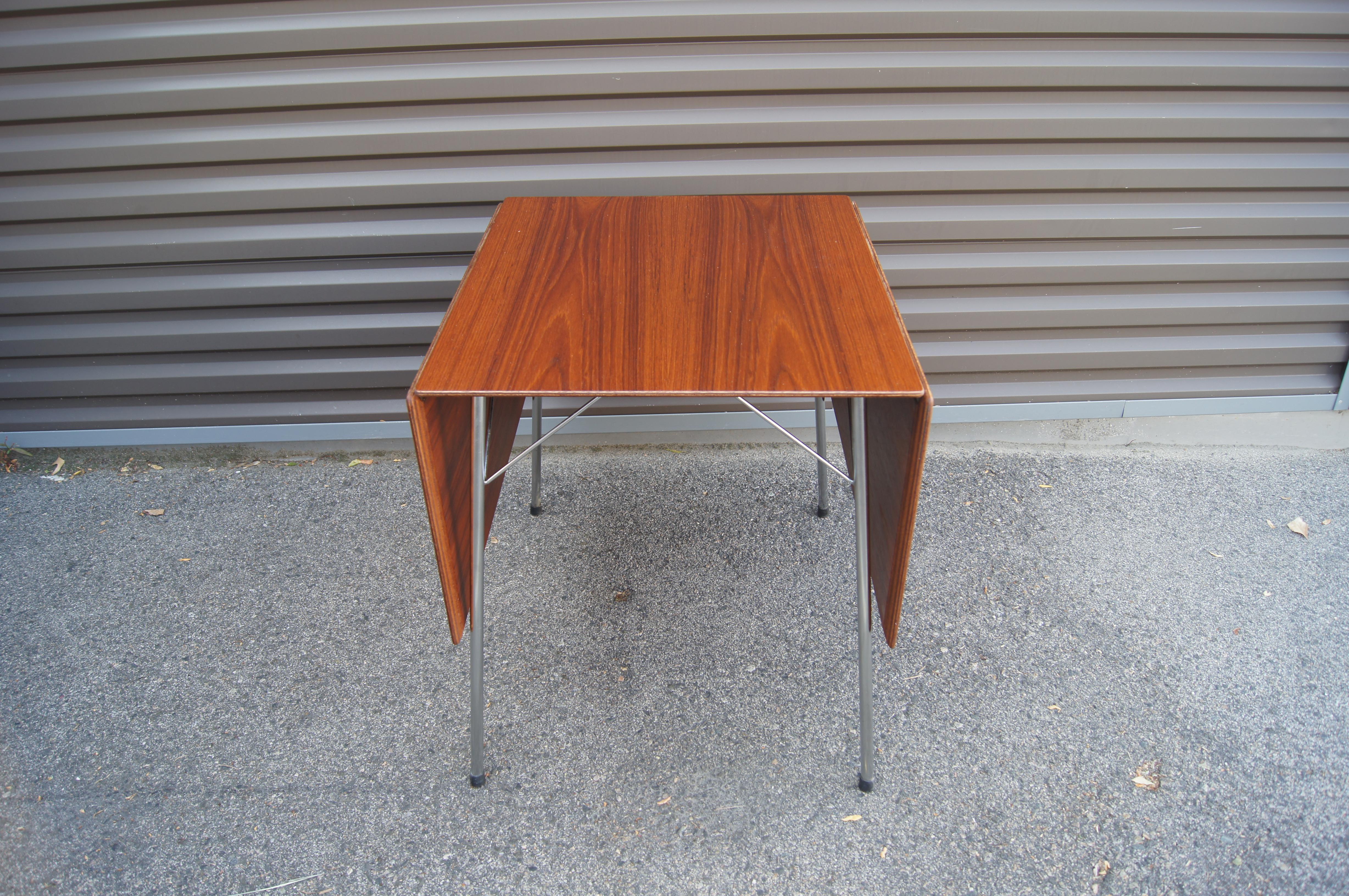 Dieser schlichte, skandinavisch-moderne Esstisch, Modell 3601, wurde 1952 von Arne Jacobsen für Fritz Hansen entworfen und verfügt über eine Platte aus Teakholz mit hängenden Blättern auf einem schlanken Gestell aus poliertem Stahl. Der Tisch, der