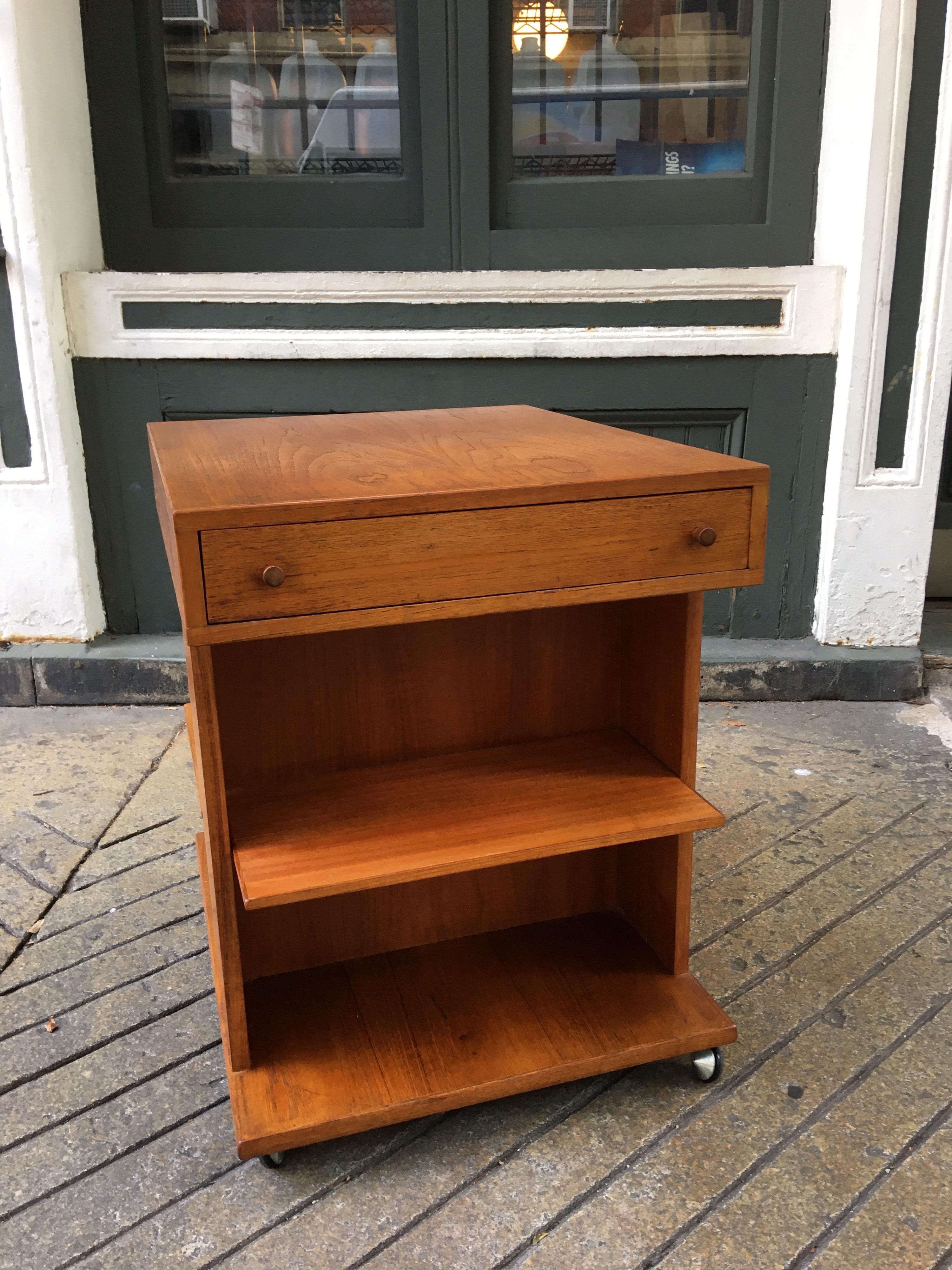 Teak end table with one-drawer and adjustable shelves. Table is on wheels which makes it easy to rotate and use in different places! Probably dates from the 1970s original condition is good! Perfect to use as a nightstand, end table or in the office!